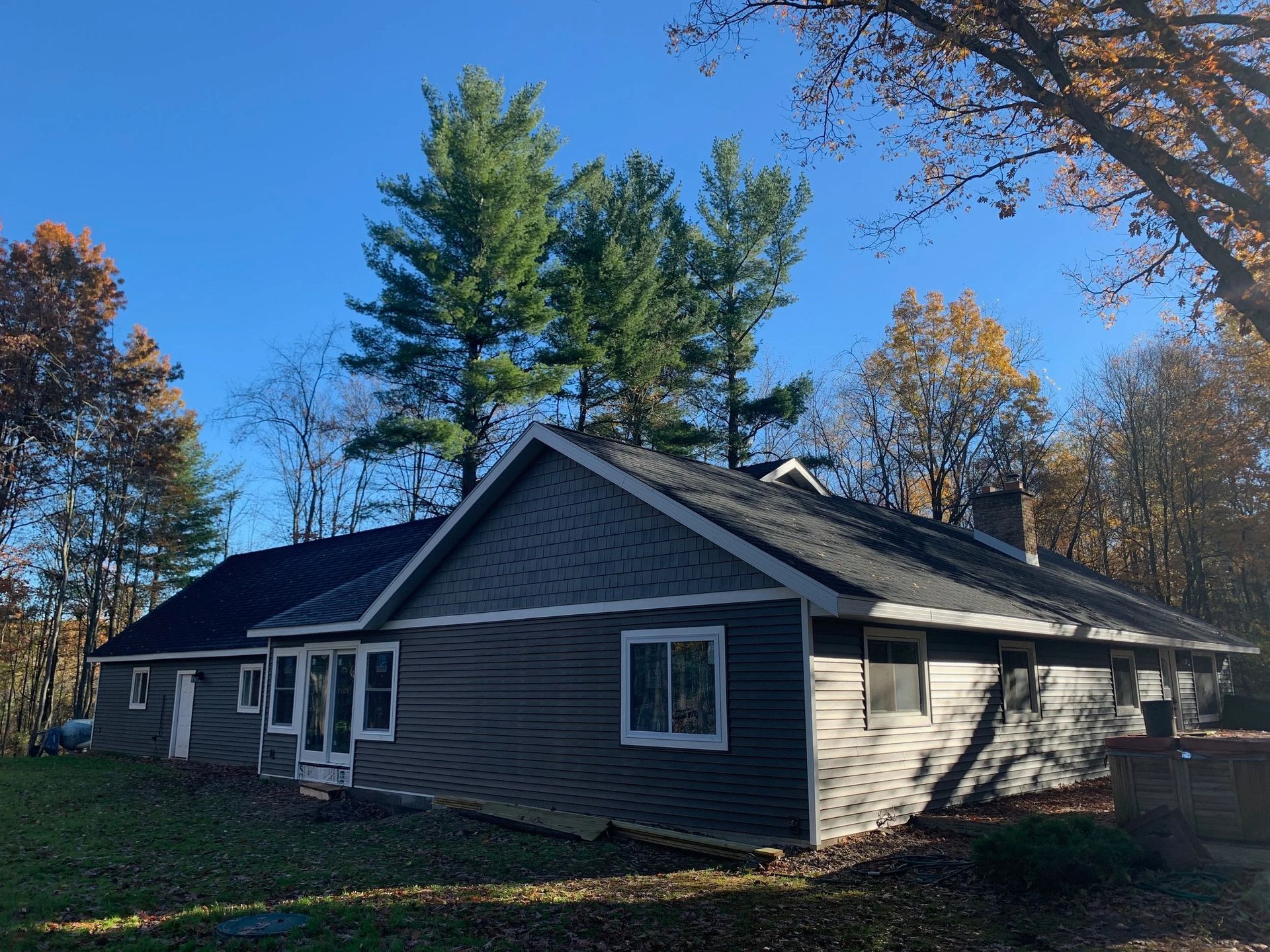 Gray house with white trim and tall trees under a clear blue sky