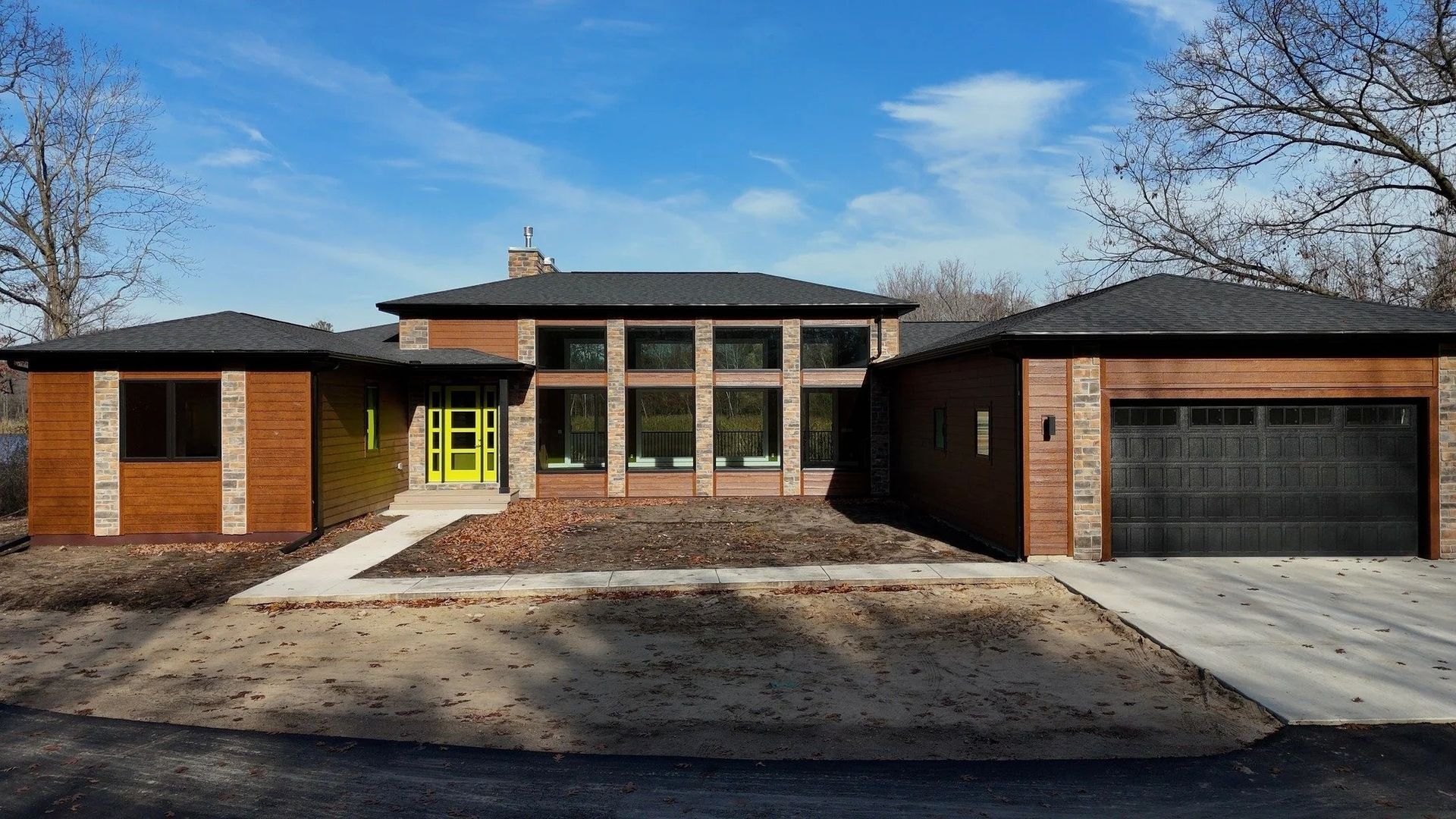 Single-story brick house with green front door, wide windows, and attached garage under a blue sky