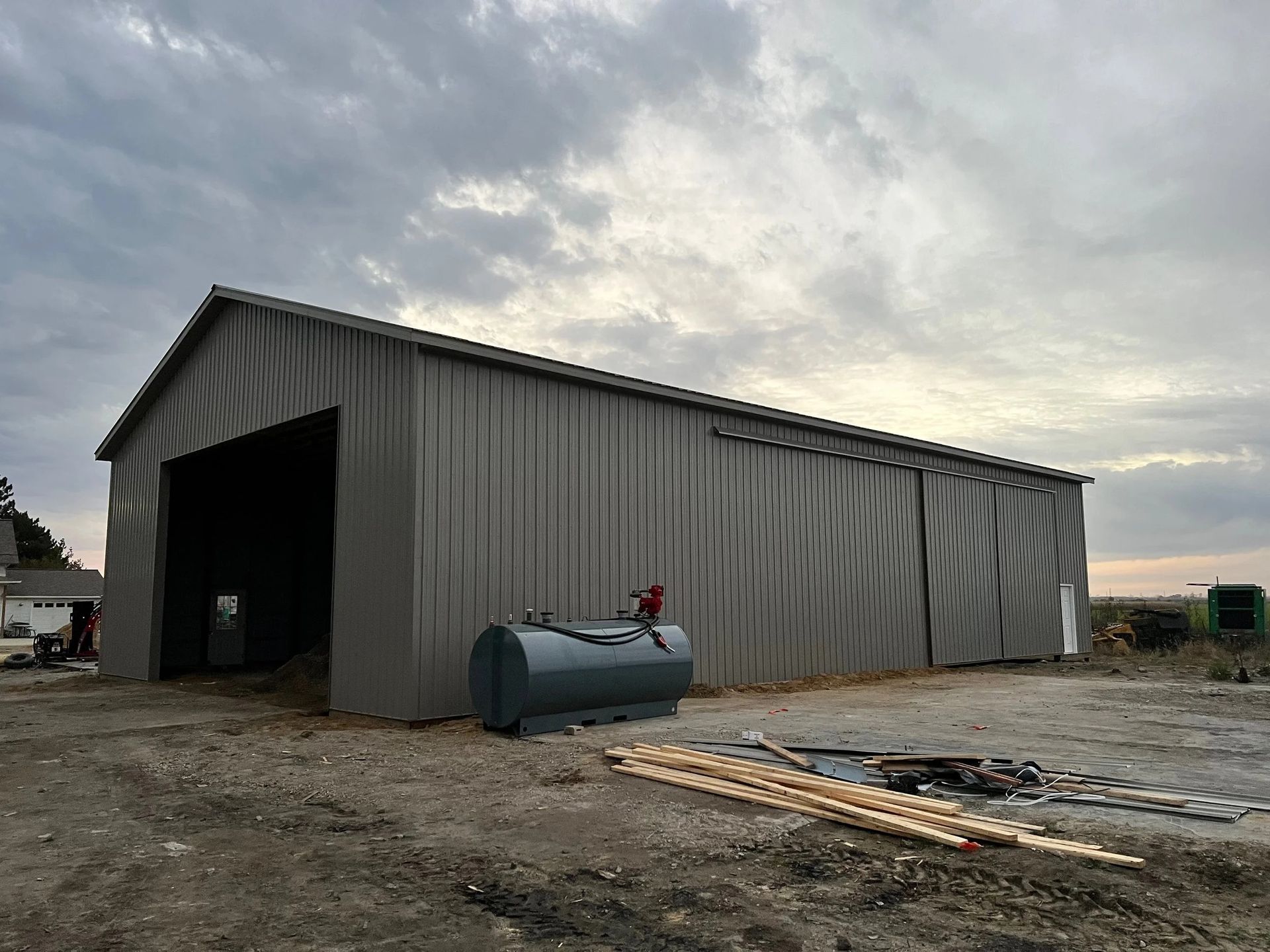 Large gray metal barn or storage shed on a gravel lot under a cloudy sky.