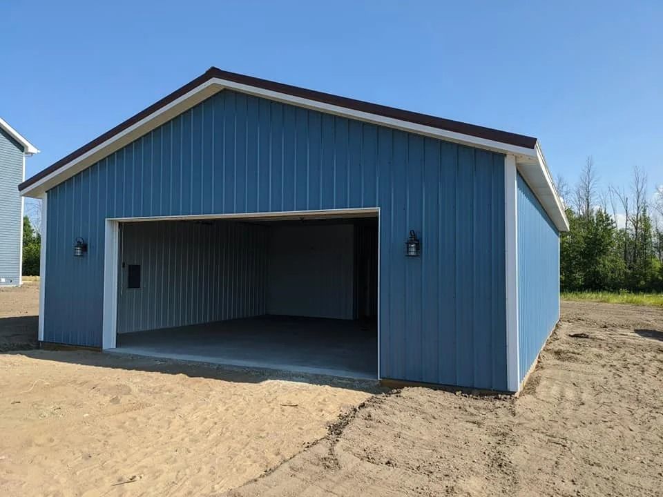 Blue detached garage with open two-car bay on a dirt lot under a clear sky