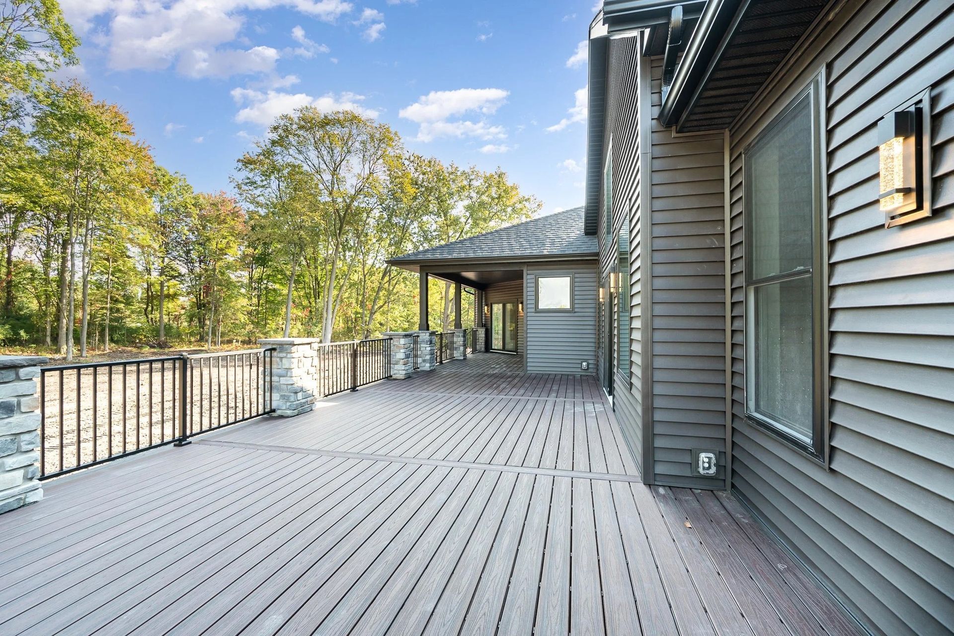 Spacious gray wooden deck beside a house, with railing and trees under a blue sky.