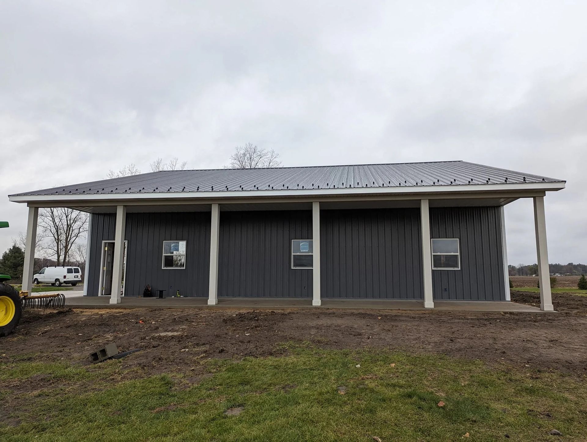 Small gray house with porch and metal roof on a muddy lot under an overcast sky