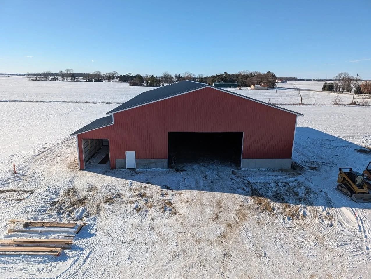 Red barn in a snowy field with open garage doors under a clear blue sky