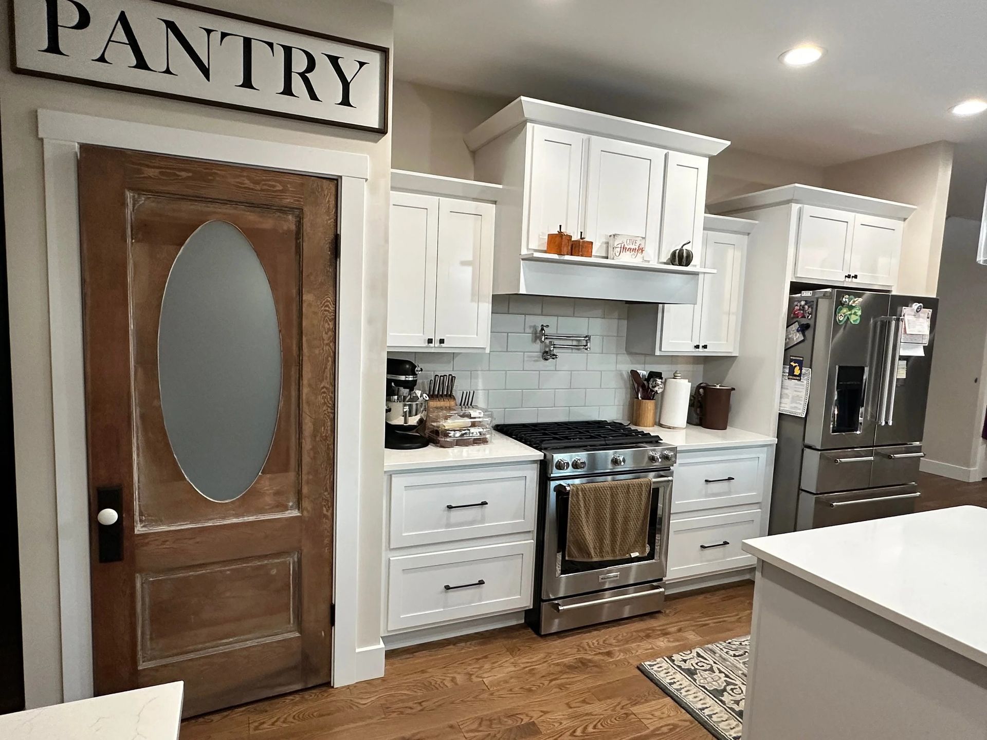Kitchen with white cabinets, stainless stove and fridge, wooden pantry door, and hardwood floor.