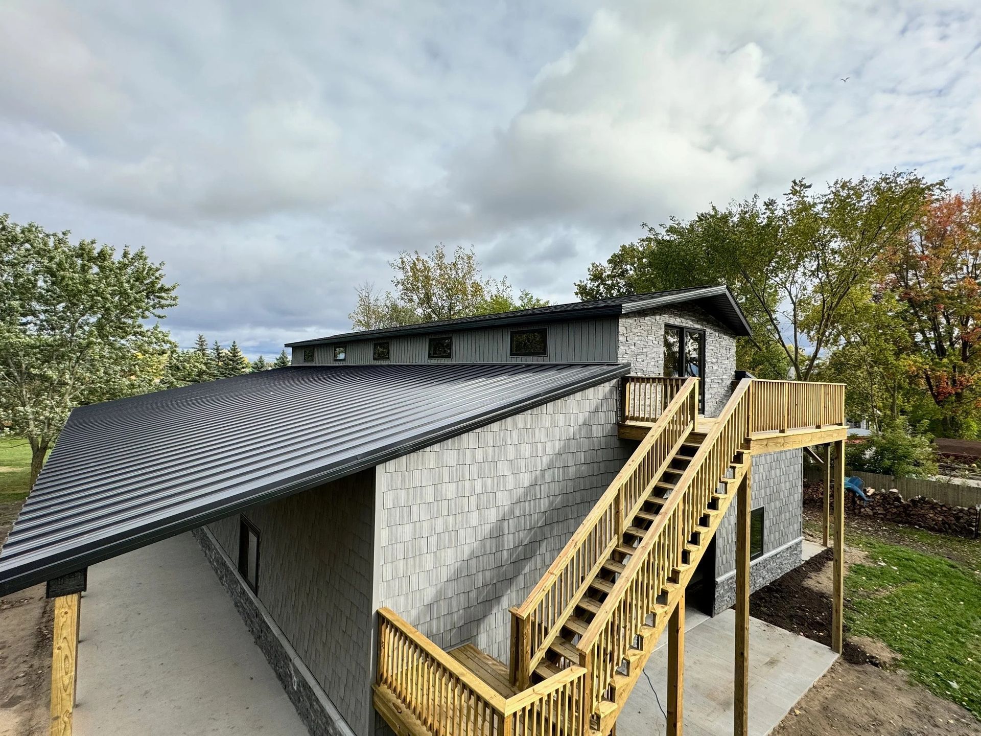 Two-story building with black roof, exterior stairs, and light gray walls in a grassy yard