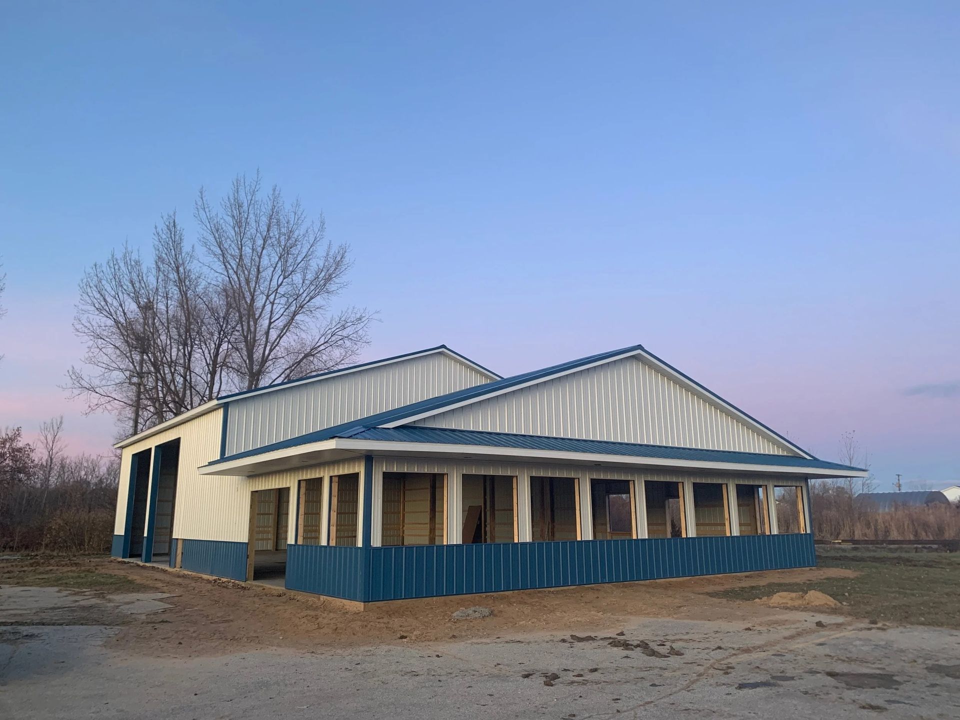 Small rural building with blue roof and trim at dusk, surrounded by bare trees and dirt ground