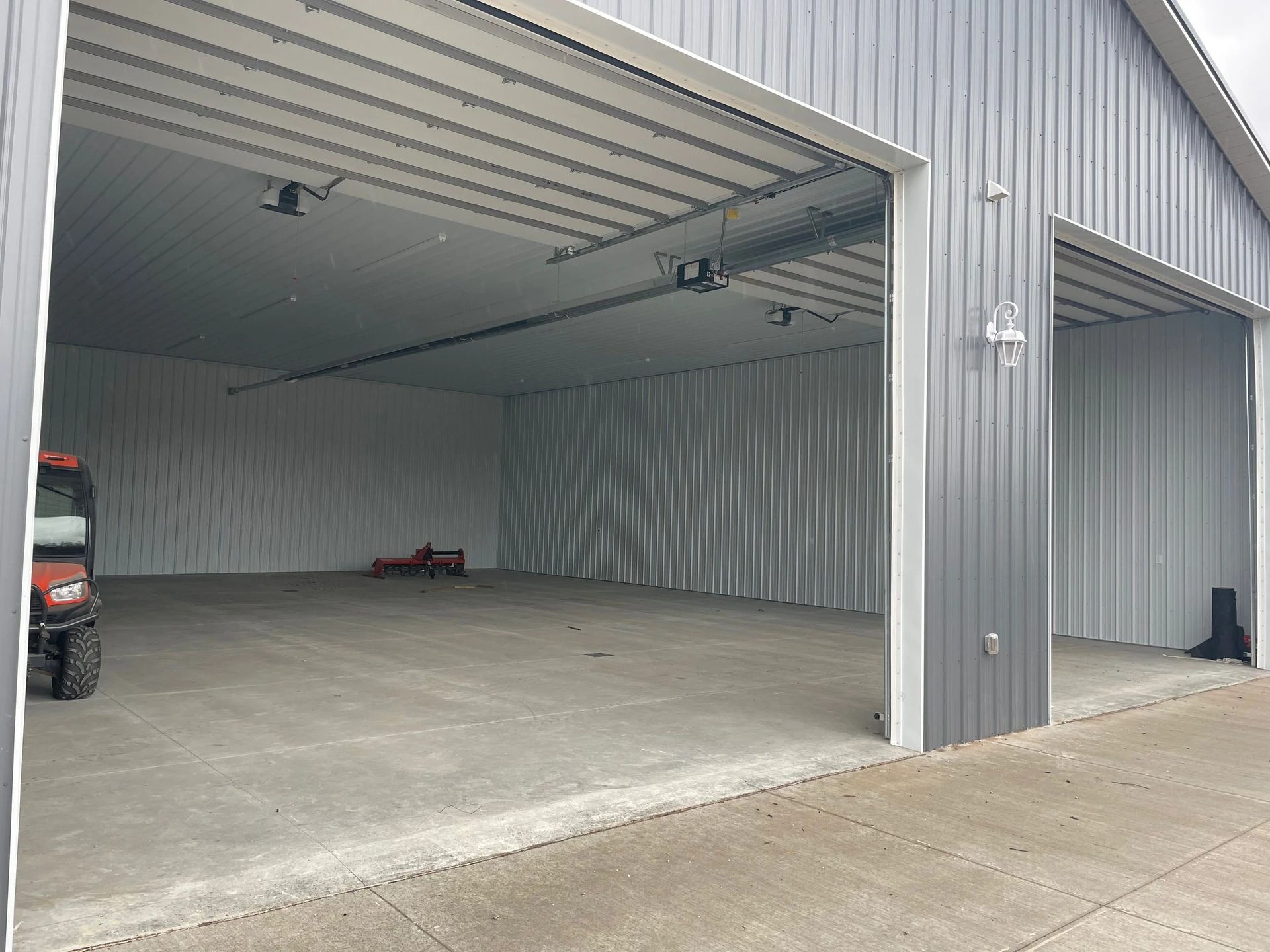 Empty metal warehouse interior with concrete floor and a parked vehicle partly visible at left