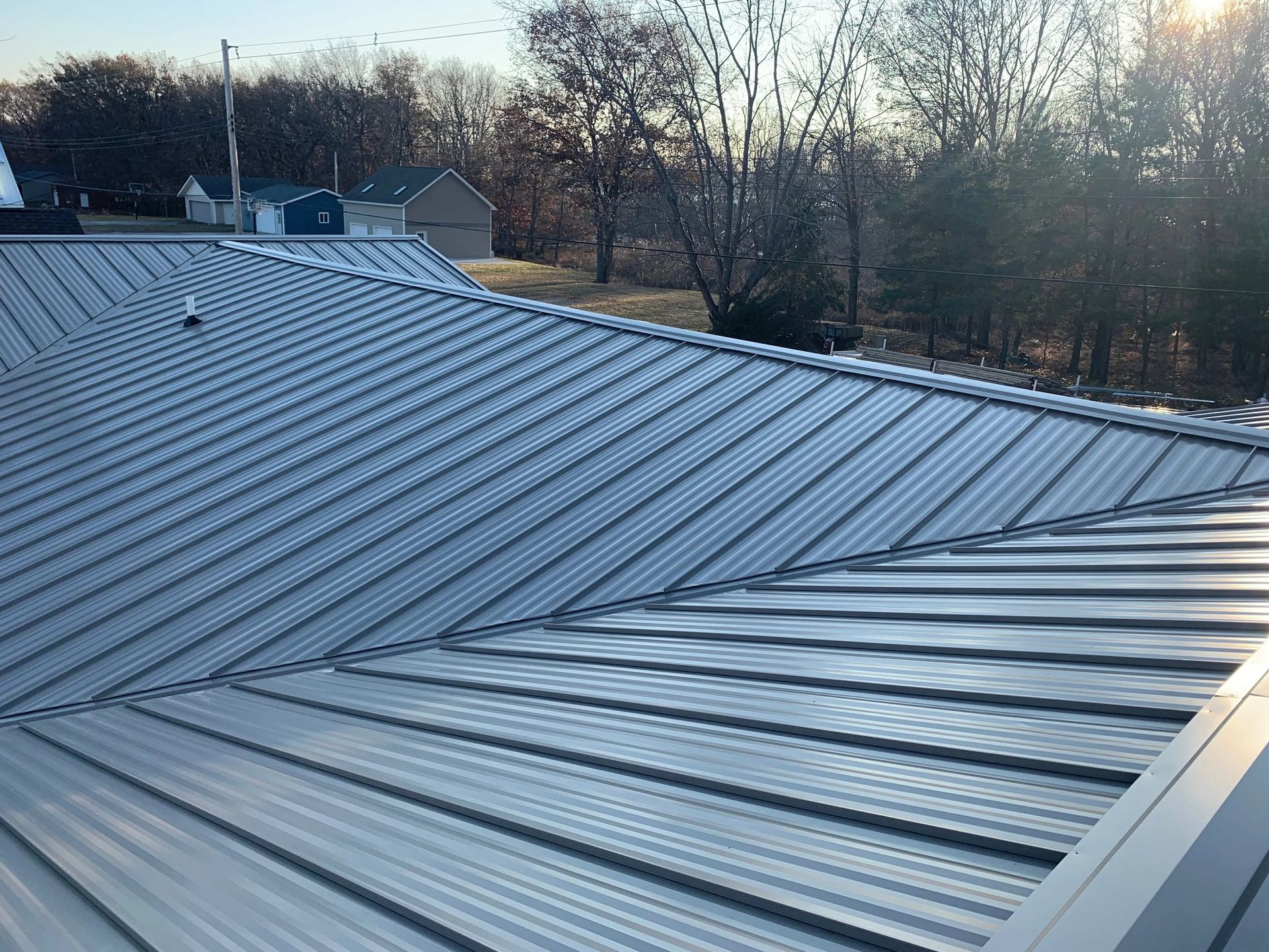 Metal roof with ridged panels in daylight, with trees and houses visible in the background