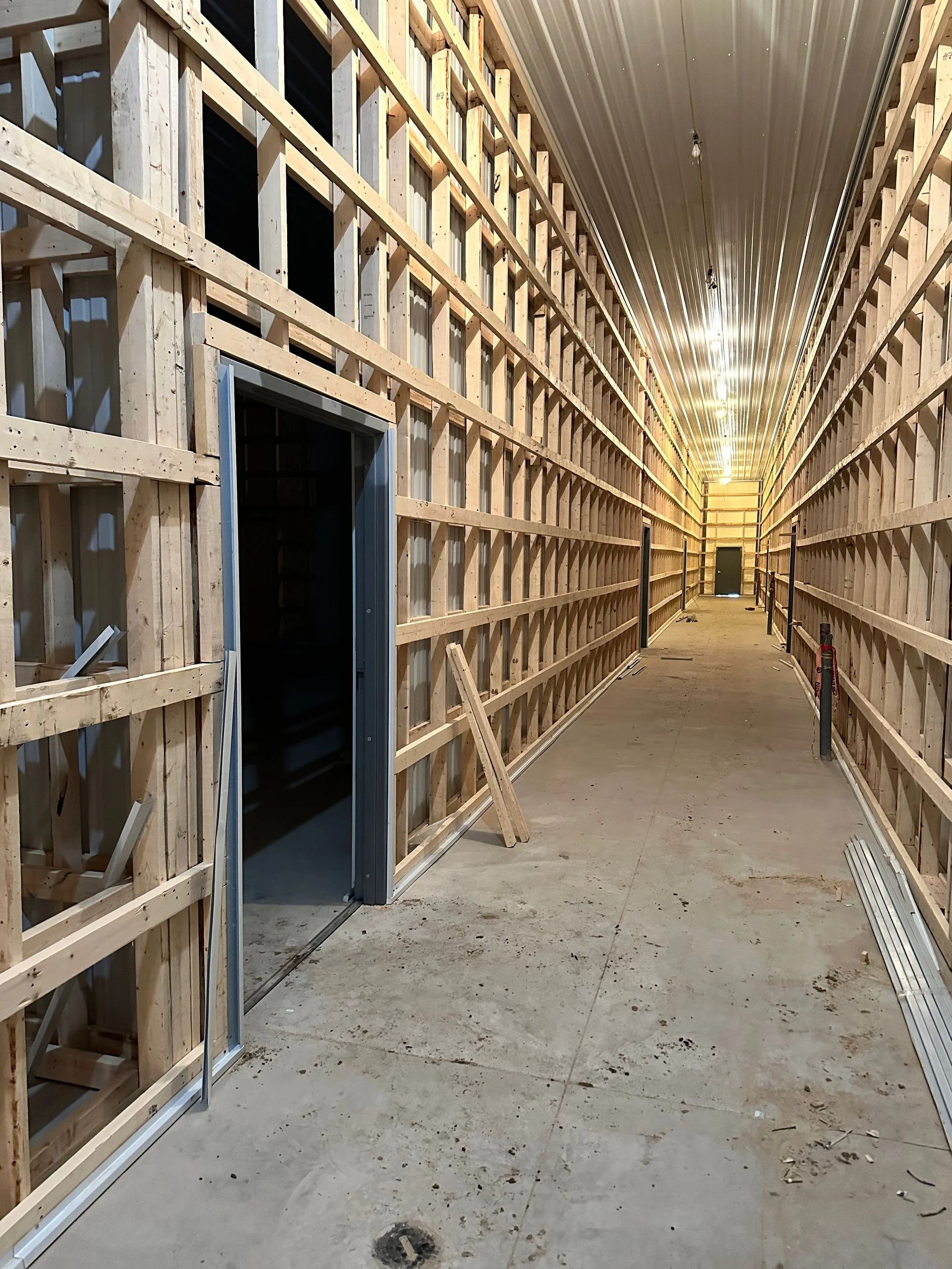 Long corridor in a building under construction, with exposed wooden framing and a concrete floor.
