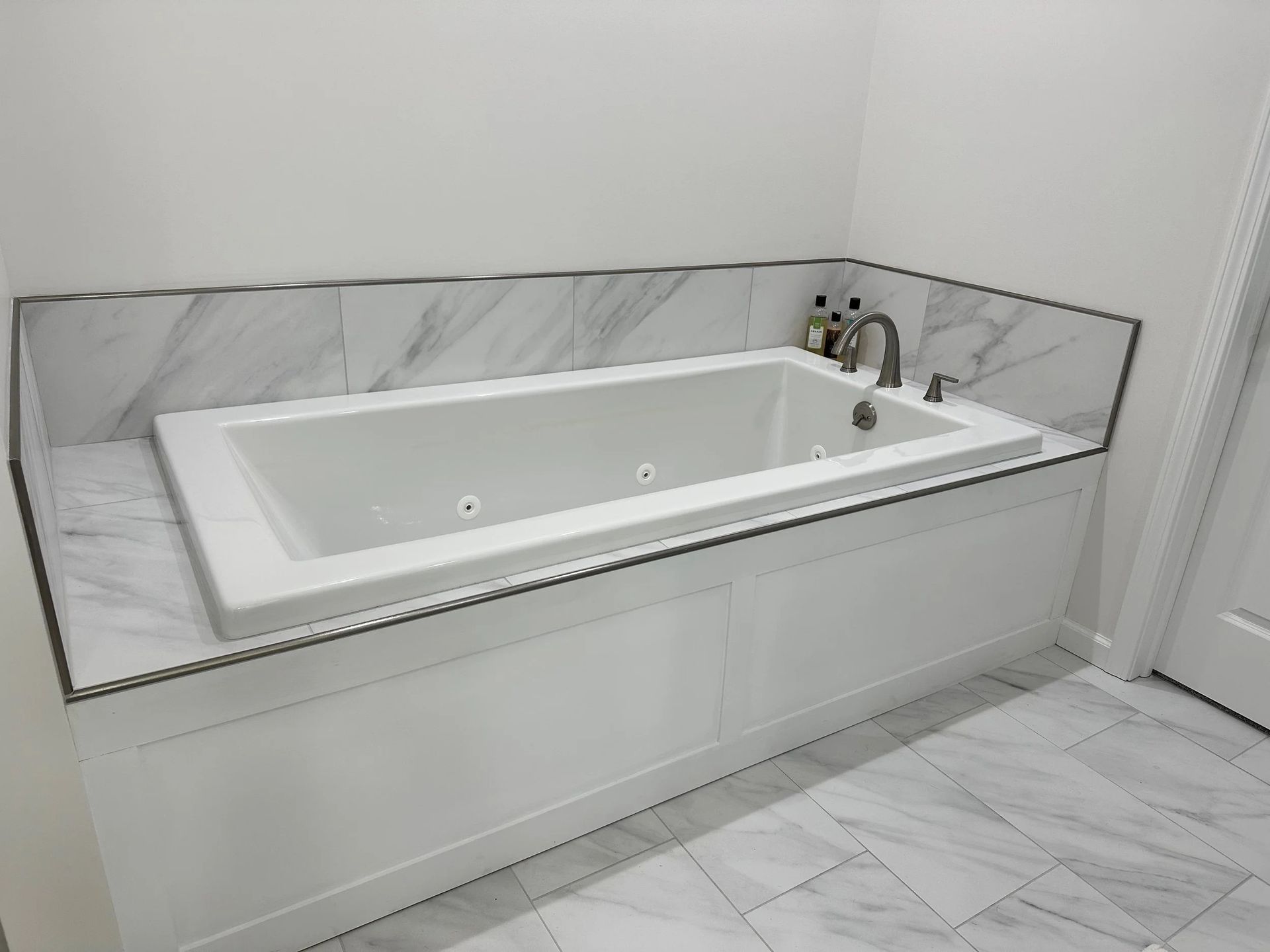 Modern bathroom with a white built-in soaking tub, marble tile, and chrome faucet fixtures