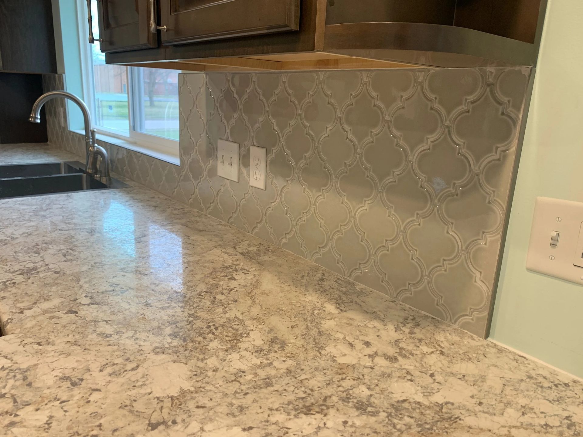 Kitchen countertop with gray-white granite, mosaic tile backsplash, window, and sink faucet