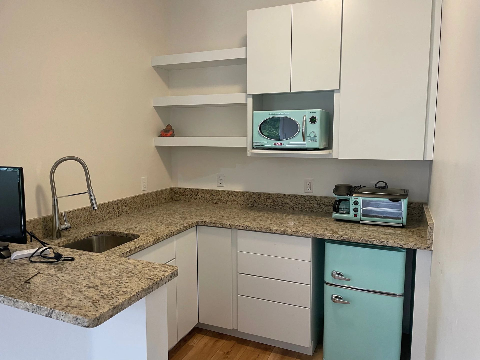 Small kitchen with white cabinets, granite counters, turquoise mini fridge, and microwave on a shelf.