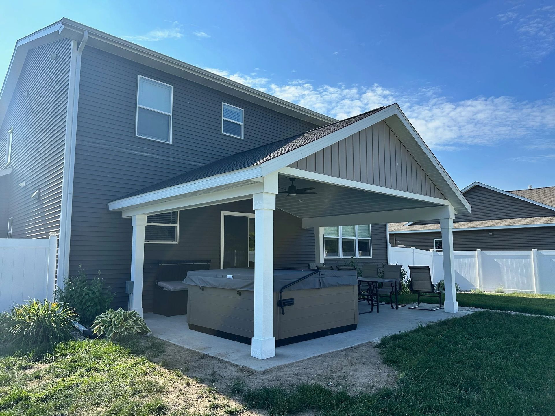 Backyard patio with white-roofed pergola beside a gray two-story house and lawn