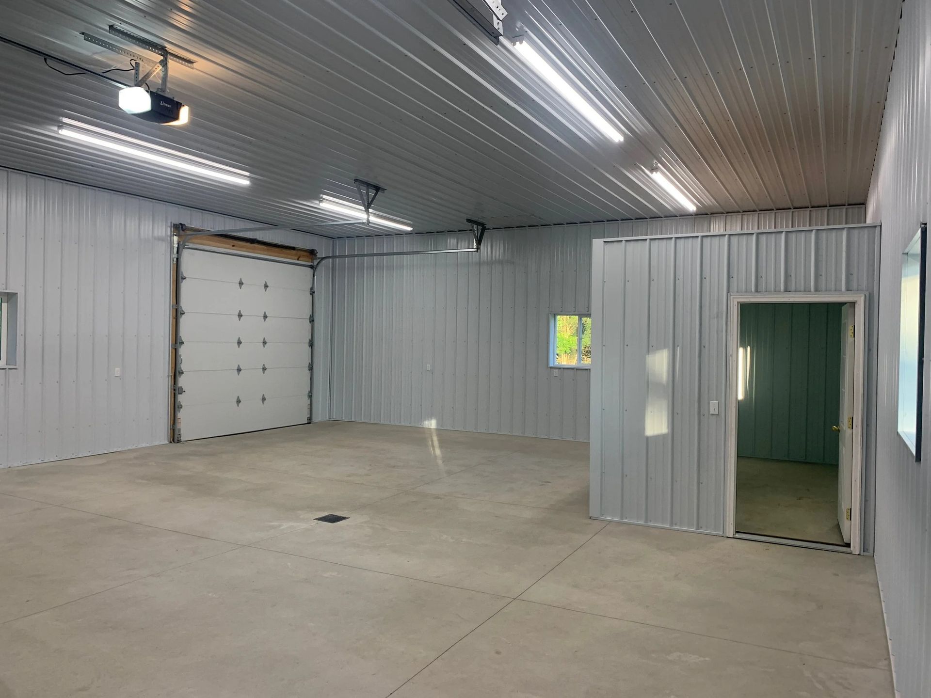 Empty industrial garage with concrete floor, white metal walls, and overhead lights.