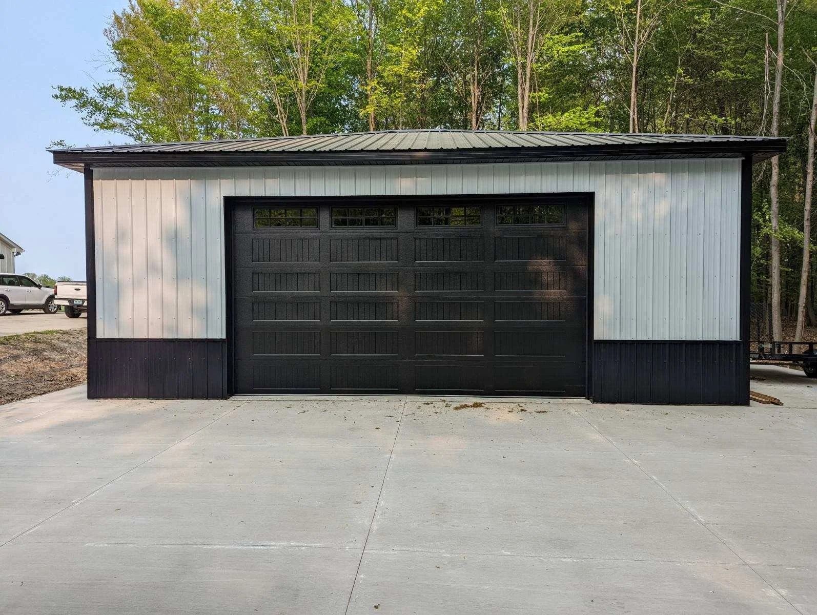 Small white-and-black garage building with a large black door on a concrete lot
