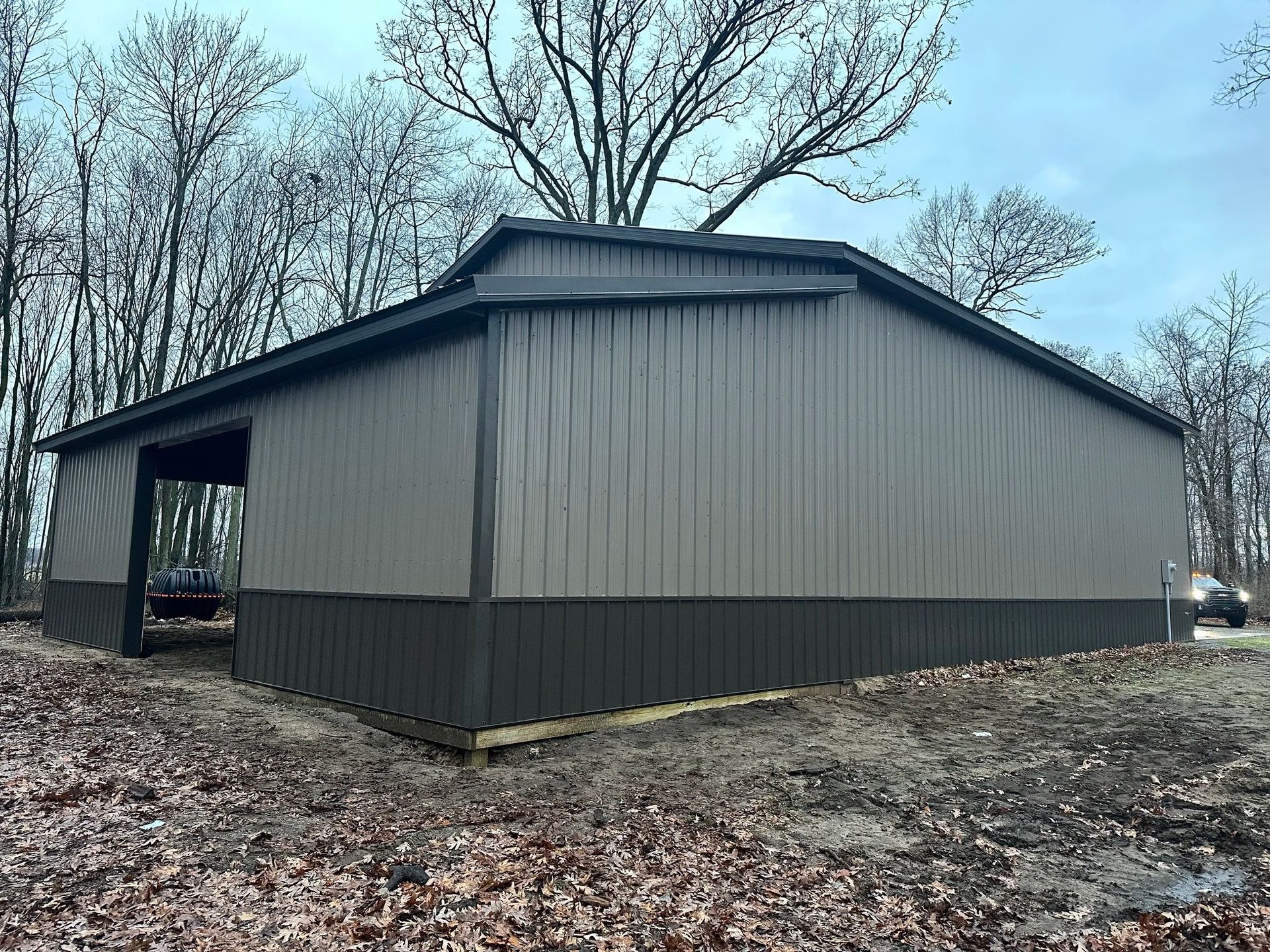 Gray metal barn with open side and leafless trees on a wooded lot