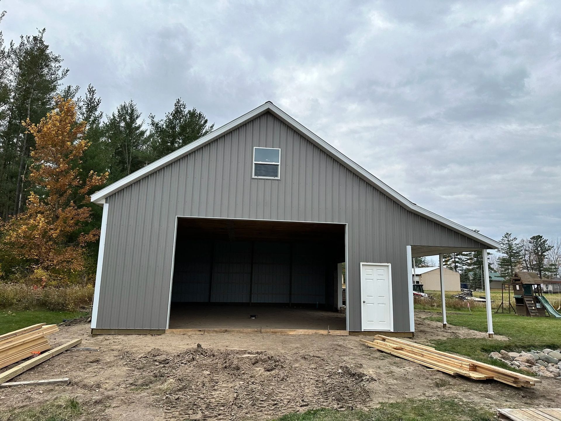 Gray metal barn with open garage door, gravel driveway, and cloudy sky