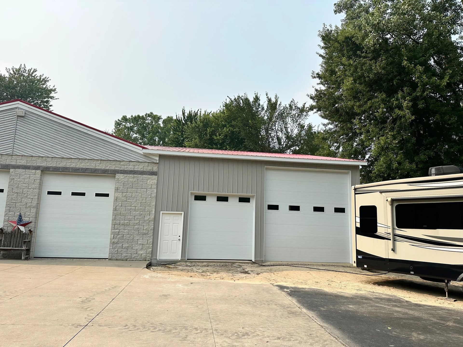 Three garage bays in a stone building, with a camper trailer parked beside them.