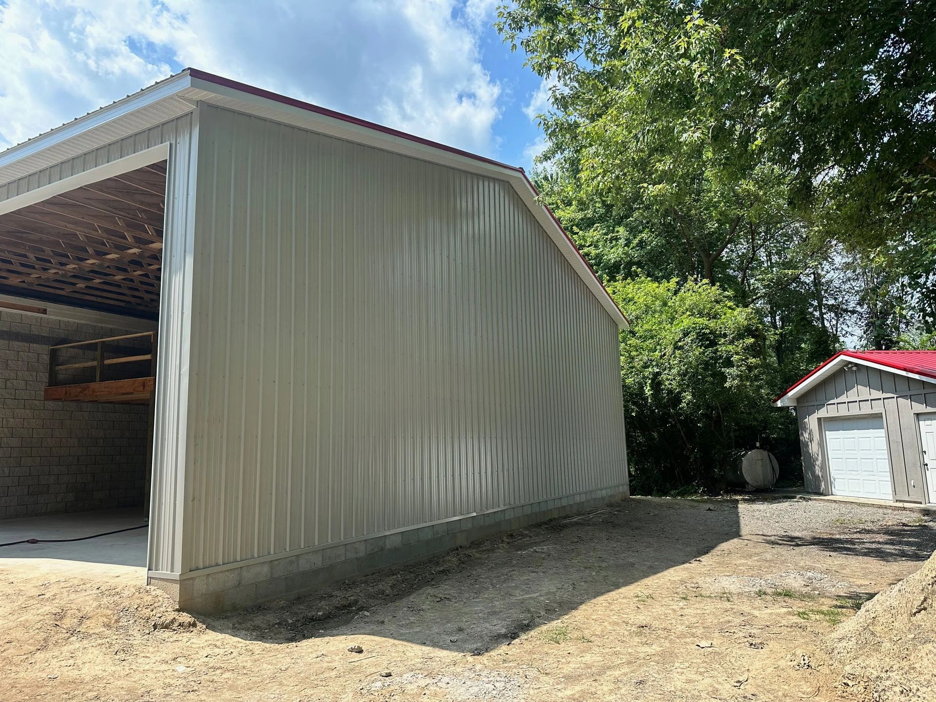 Metal-sided barn beside a gravel driveway, with a garage and trees in the background.