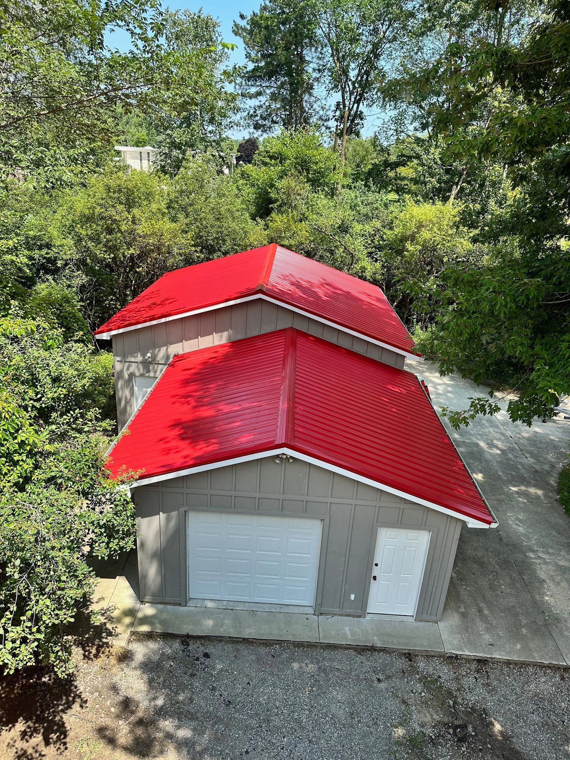 Small gray house with bright red roofs surrounded by trees and greenery.