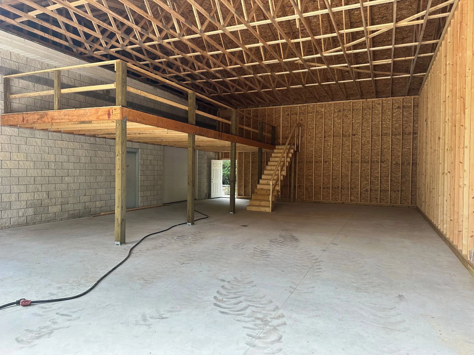 Unfinished interior with wood framing, loft stairs, exposed ceiling, and concrete floor under construction