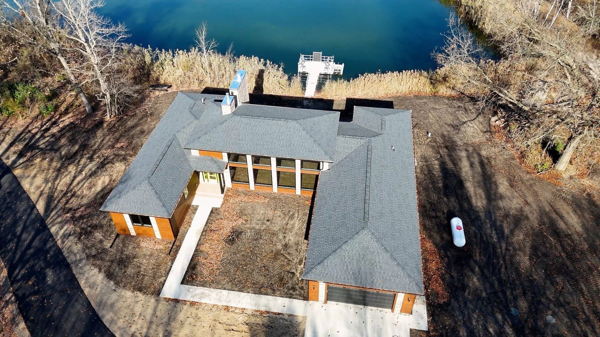 Aerial view of a gray-roofed lakeside house with a central courtyard and bare trees nearby.