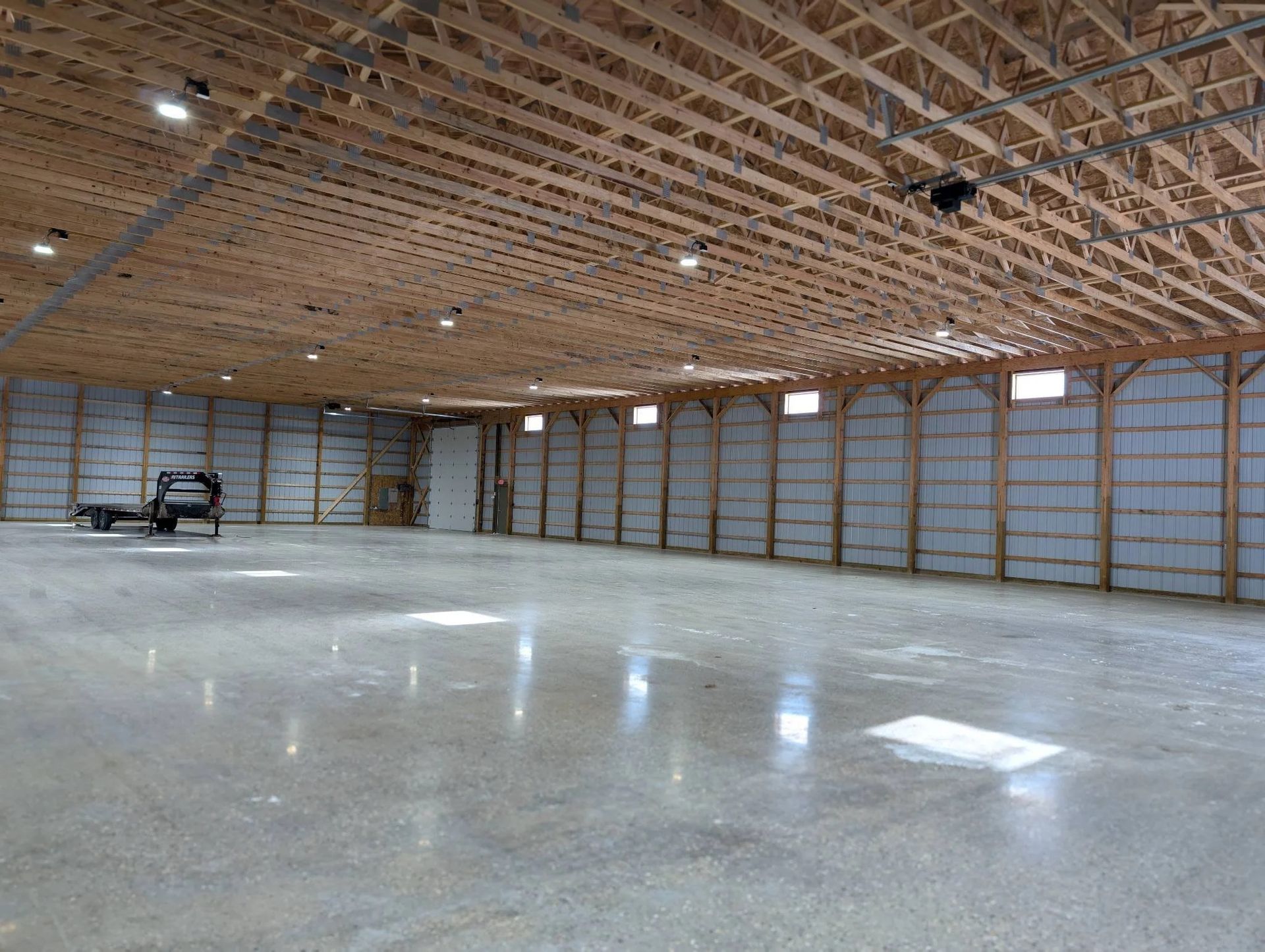 Large empty indoor hall with polished concrete floor, exposed wood roof, and metal wall panels