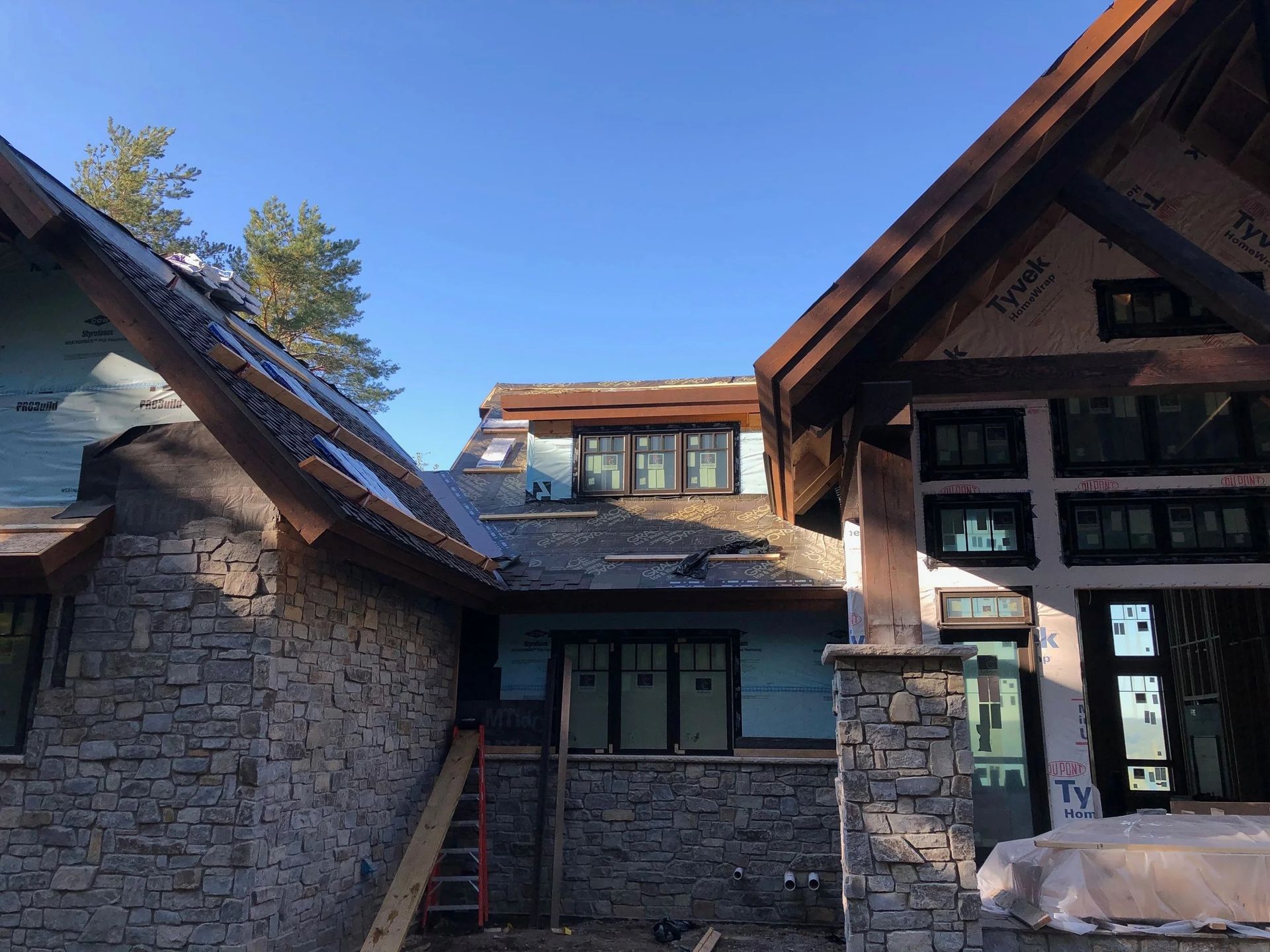 Stone and wood lodge entrance under a blue sky, with sloped roofs and a small covered walkway.