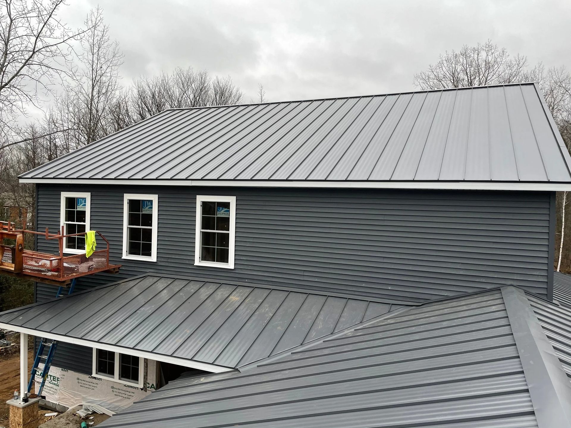 Gray metal-roofed house with dark siding and a covered porch, viewed from above in winter.