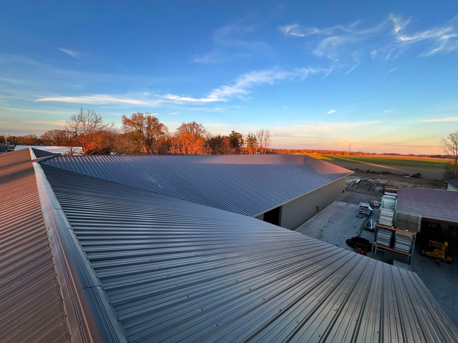 Modern rooftop with curved metal roofing at sunset, blue sky, and construction materials below
