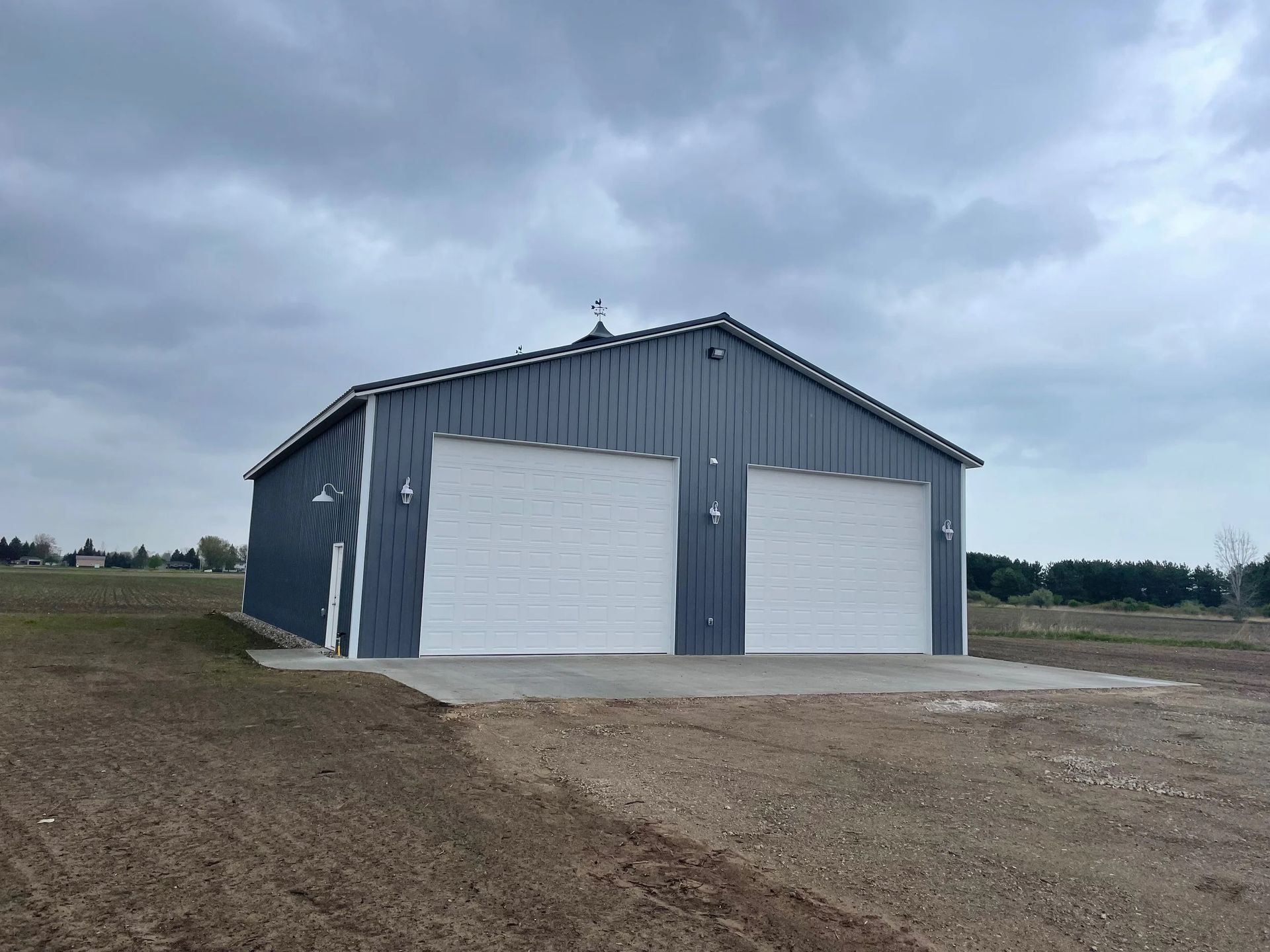 Gray metal barn with two white garage doors on a cloudy rural lot