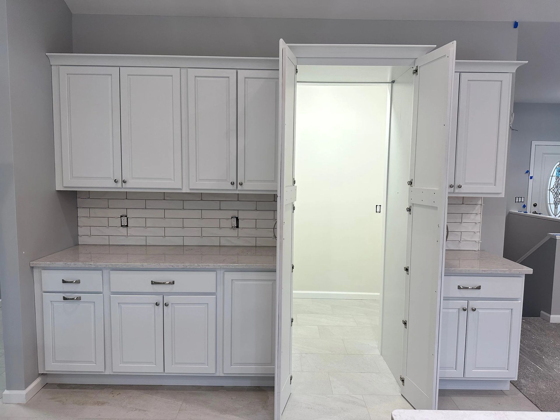 White kitchen cabinets and countertop with double French doors opening into a bright hallway
