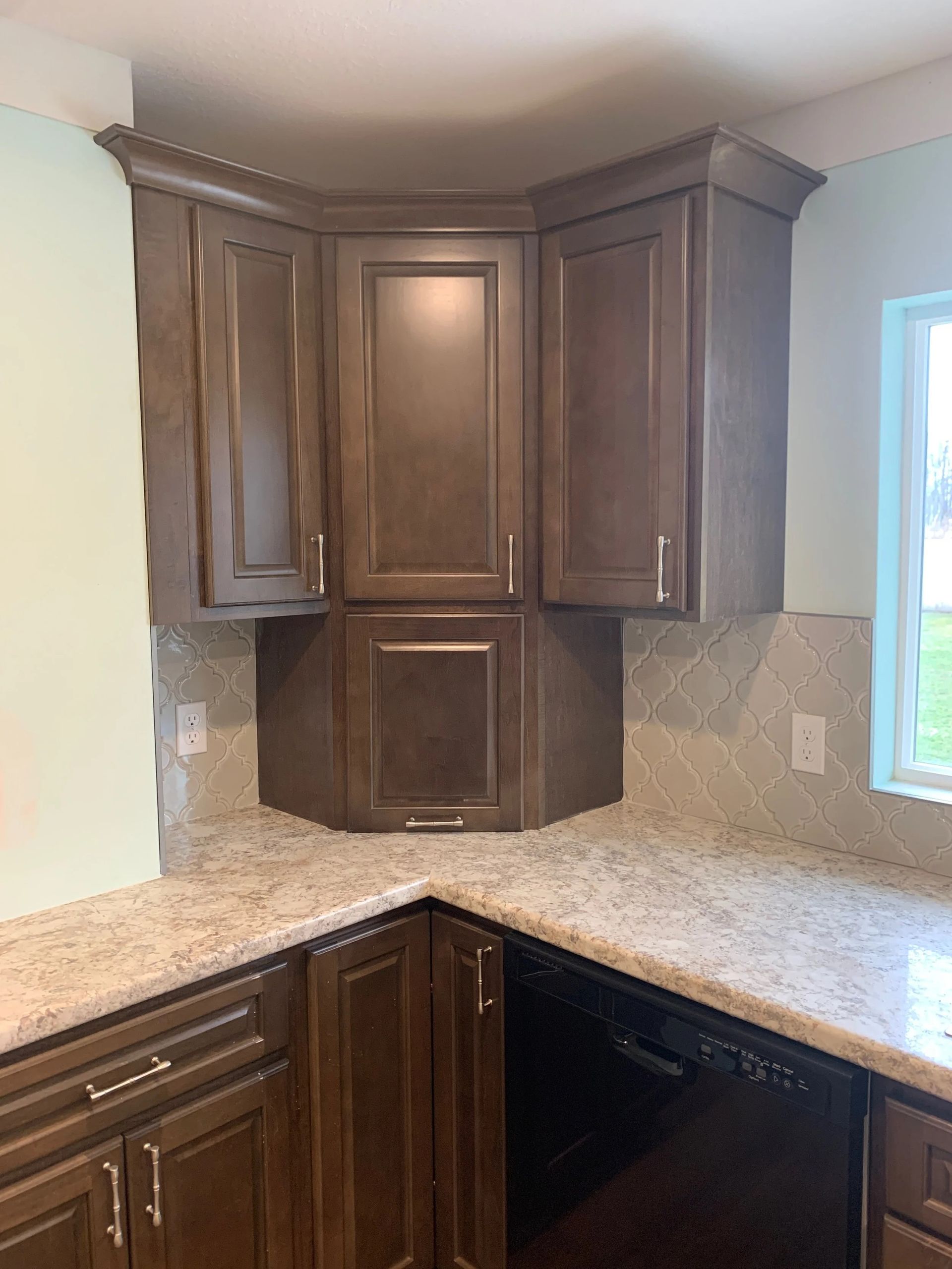 Corner kitchen with dark wood cabinets and light granite countertops, including a bright window on the right.