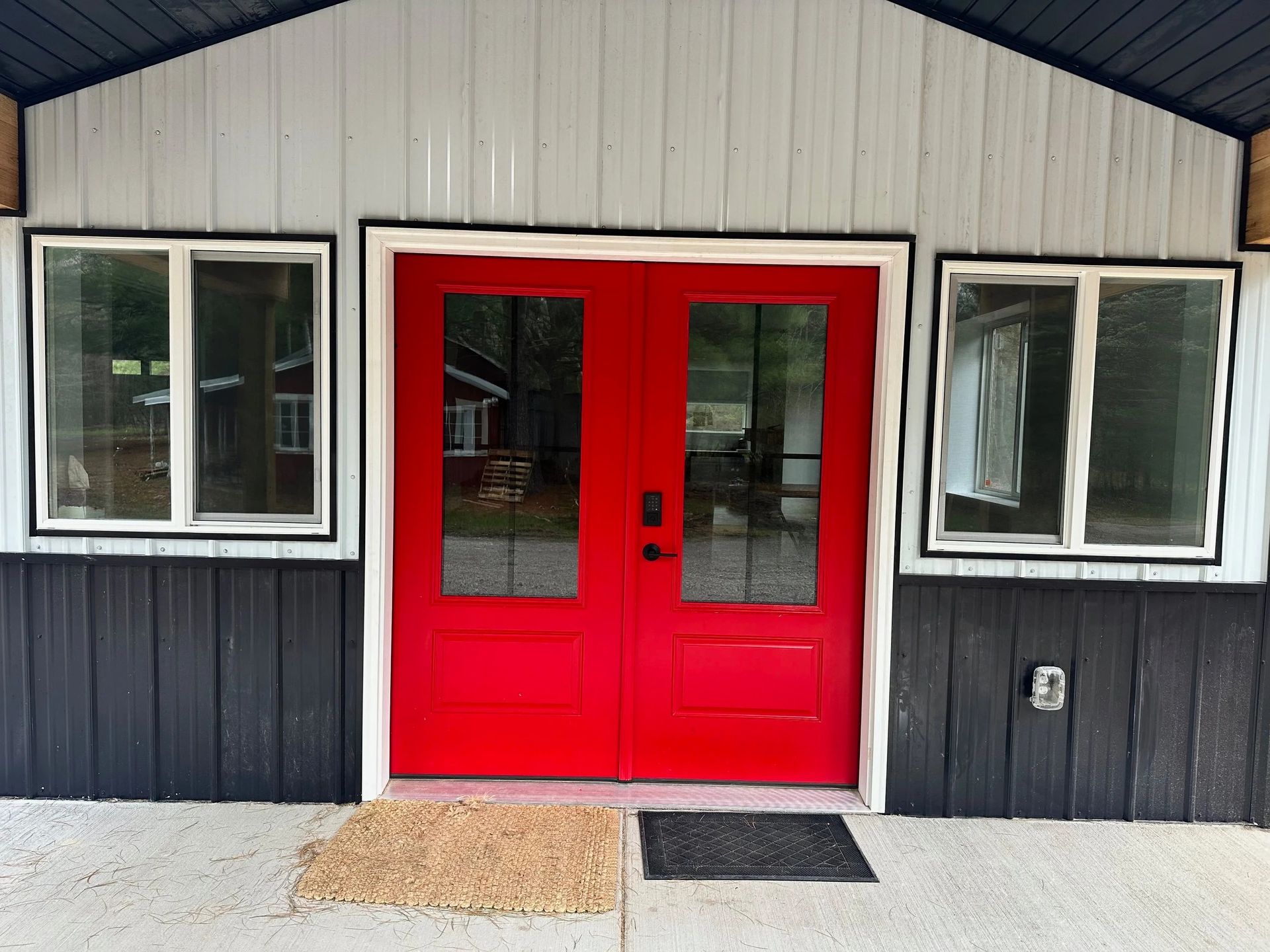 Red double doors centered on a small building facade with white-framed windows and dark siding.
