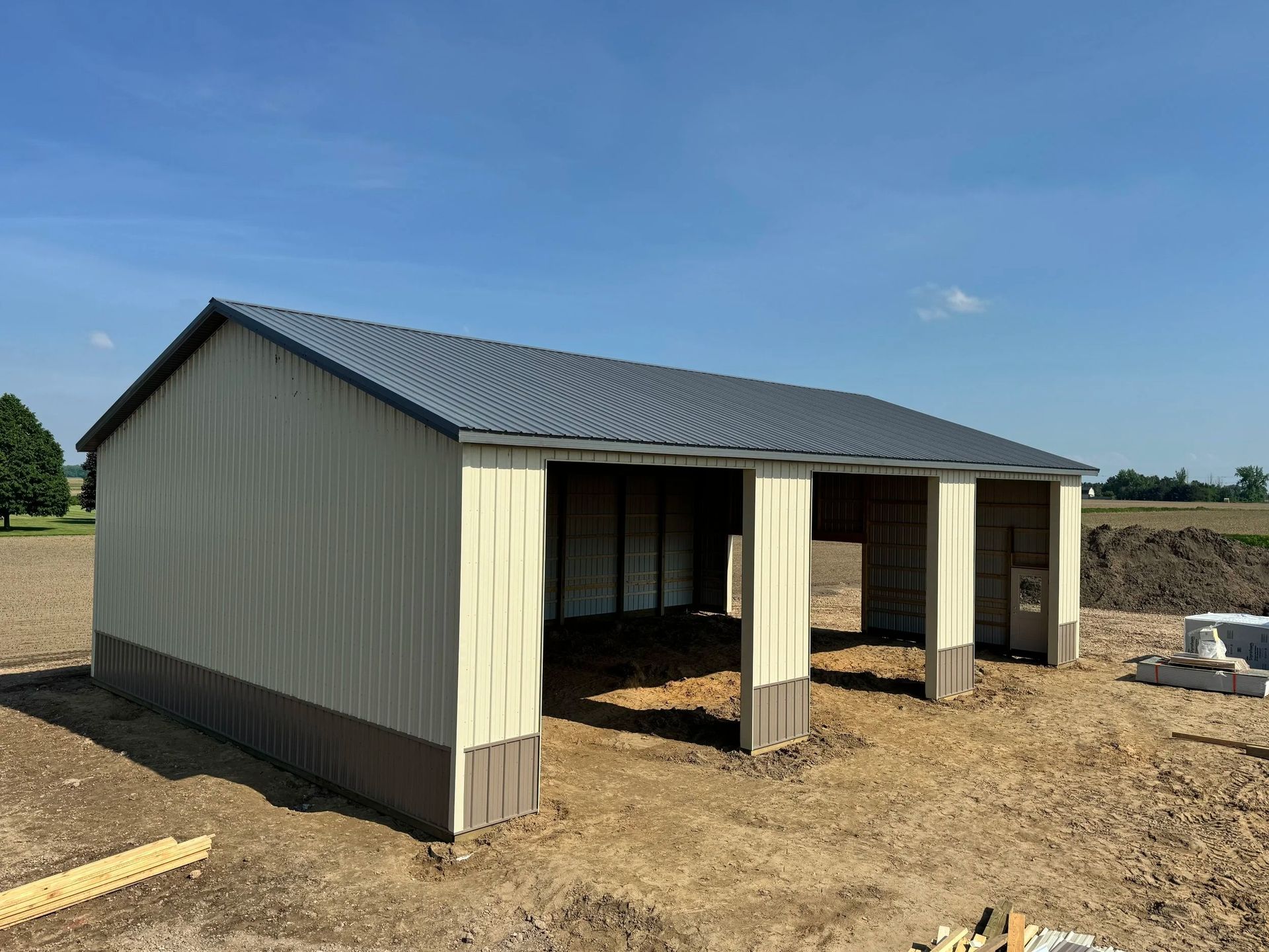 Small metal shed with open front bays on a dirt lot under a blue sky