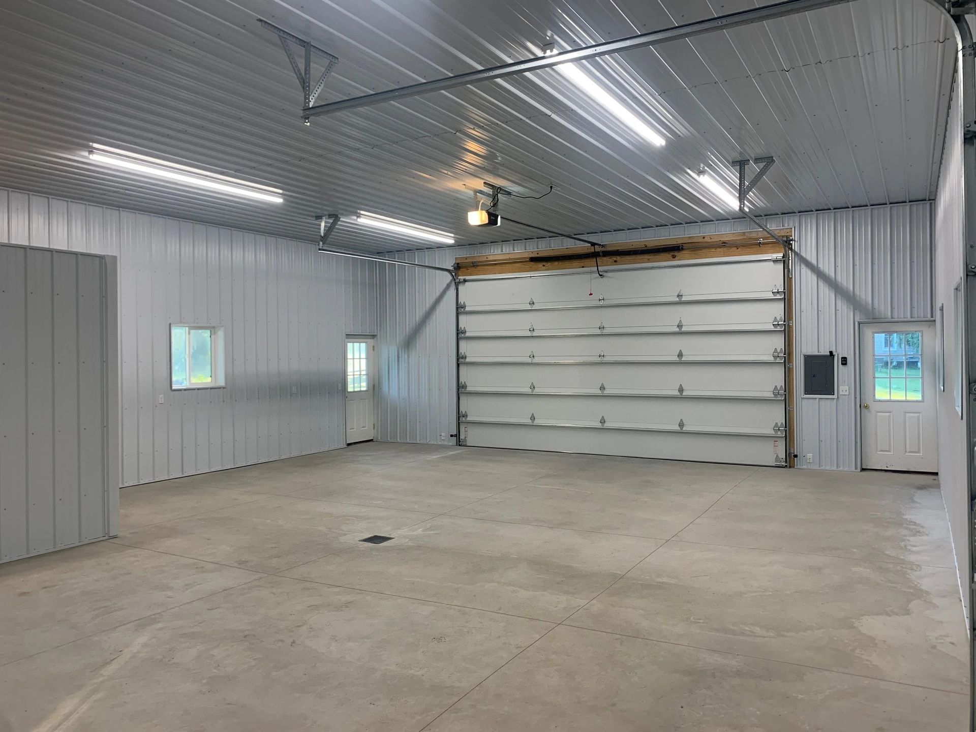 Empty metal garage with concrete floor and large white overhead door.