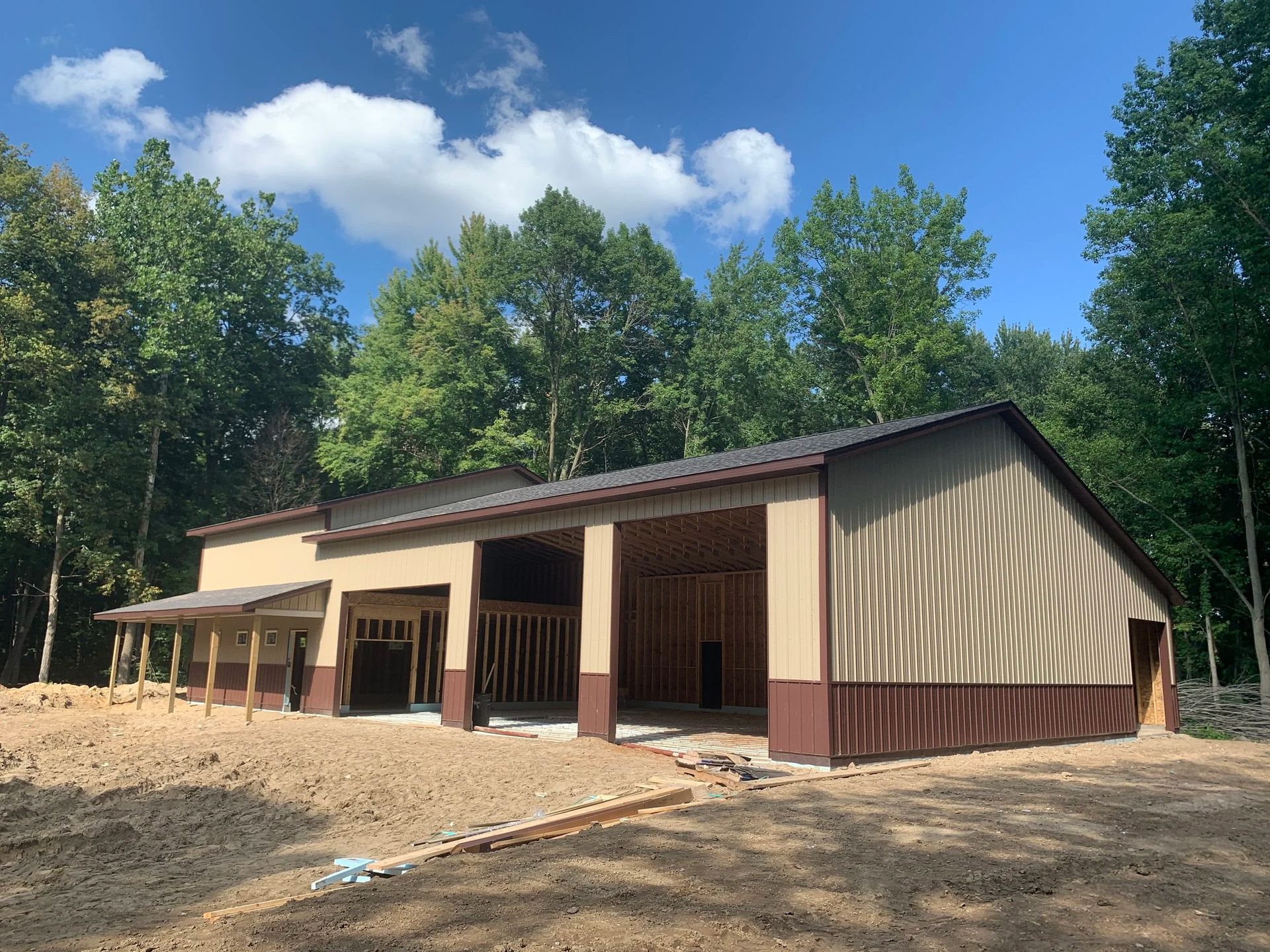 Tan and brown barn-style building under construction surrounded by trees and blue sky
