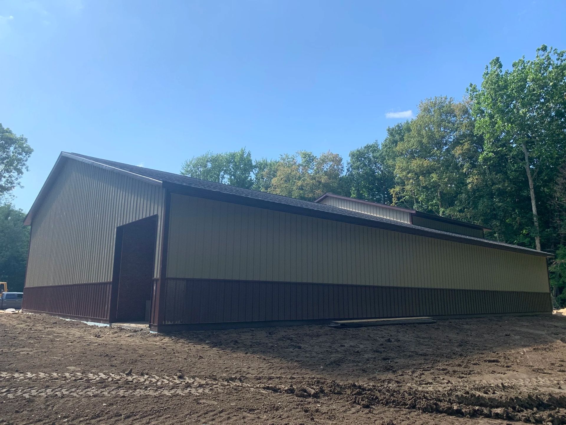 Long metal barn with open doorway beside trees under a clear blue sky.