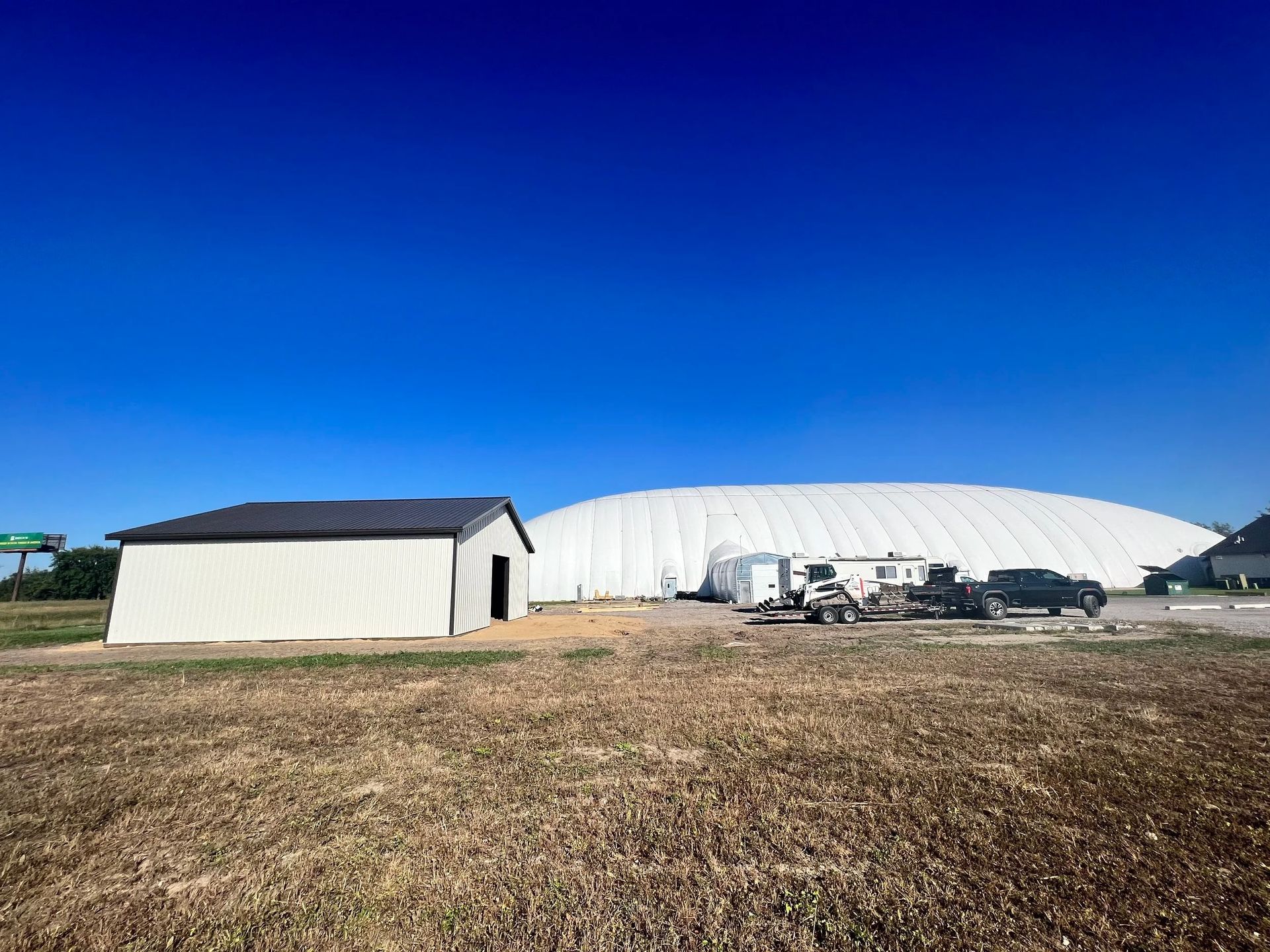 White dome building and shed in a dry field under a clear blue sky