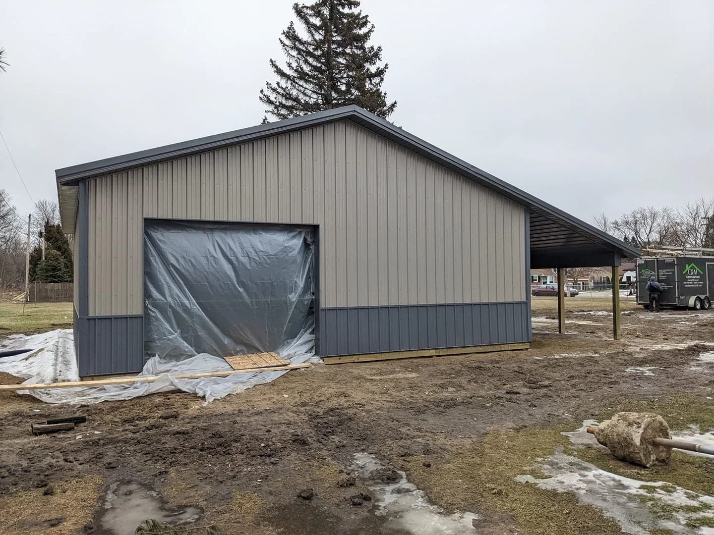 Partly finished gray metal barn with plastic-covered opening on a muddy rural lot