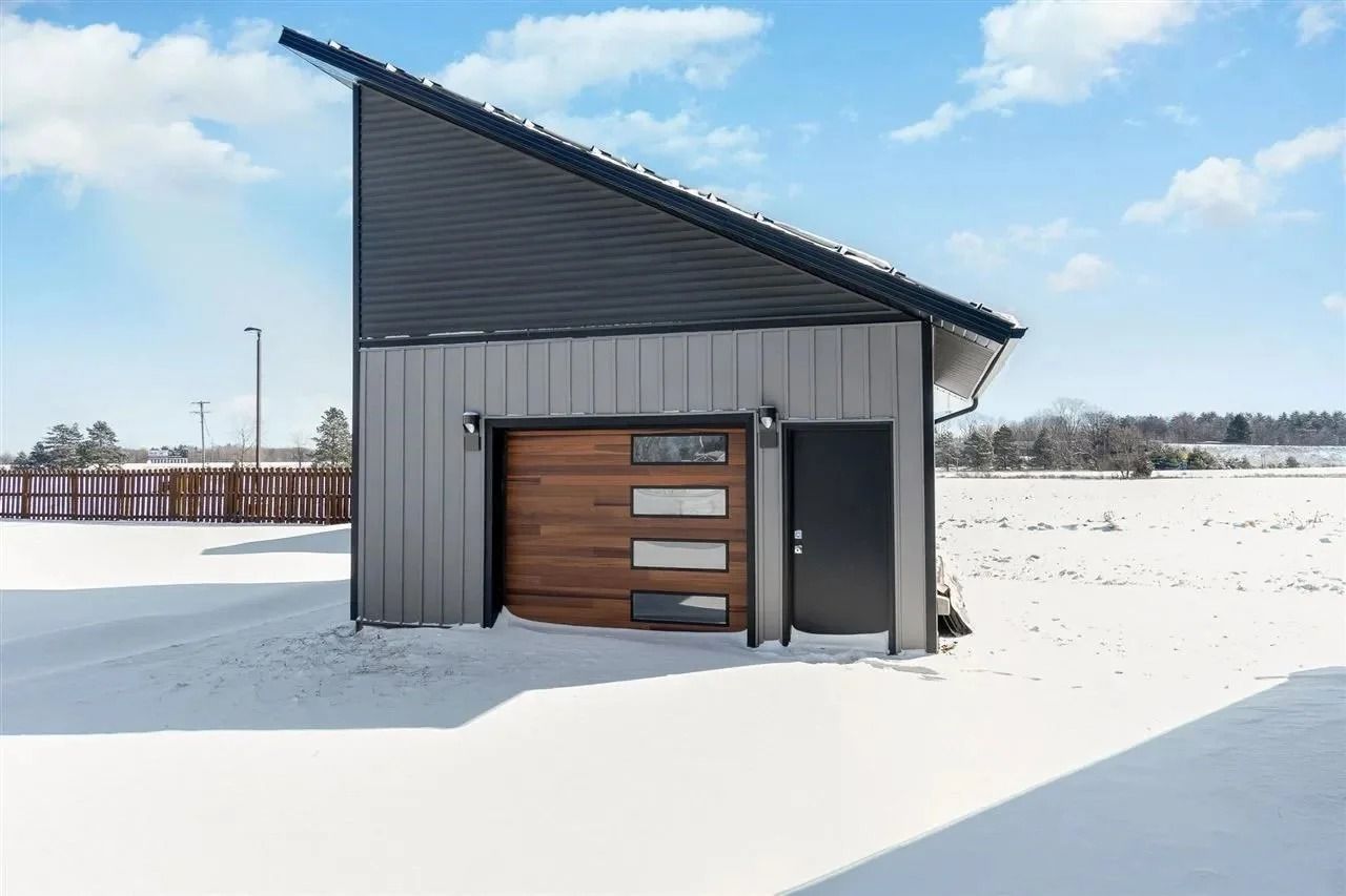 Modern gray house with wood garage door in a snowy landscape under a blue sky