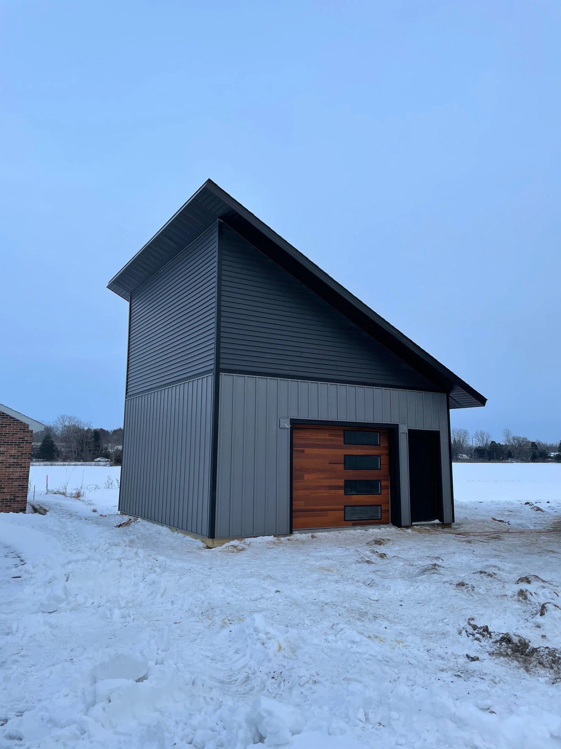 Snow-covered barn with dark siding and wooden doors under a pale sky