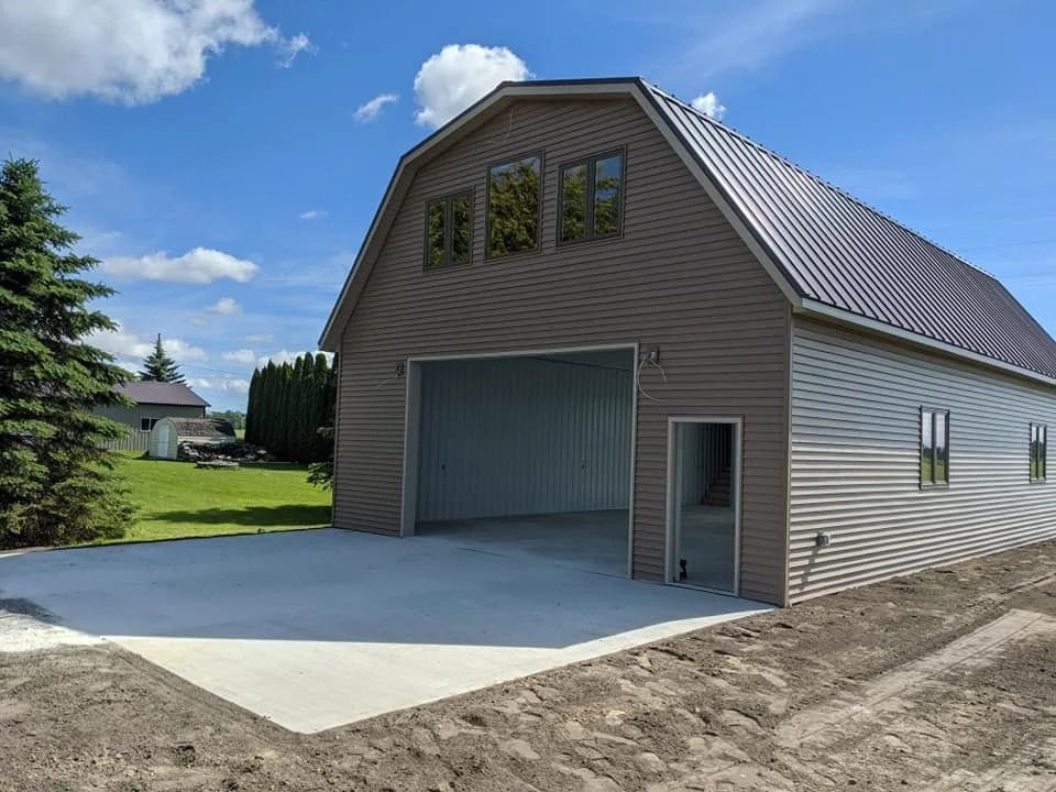 Gray metal barn with large open garage door and concrete apron under a blue sky