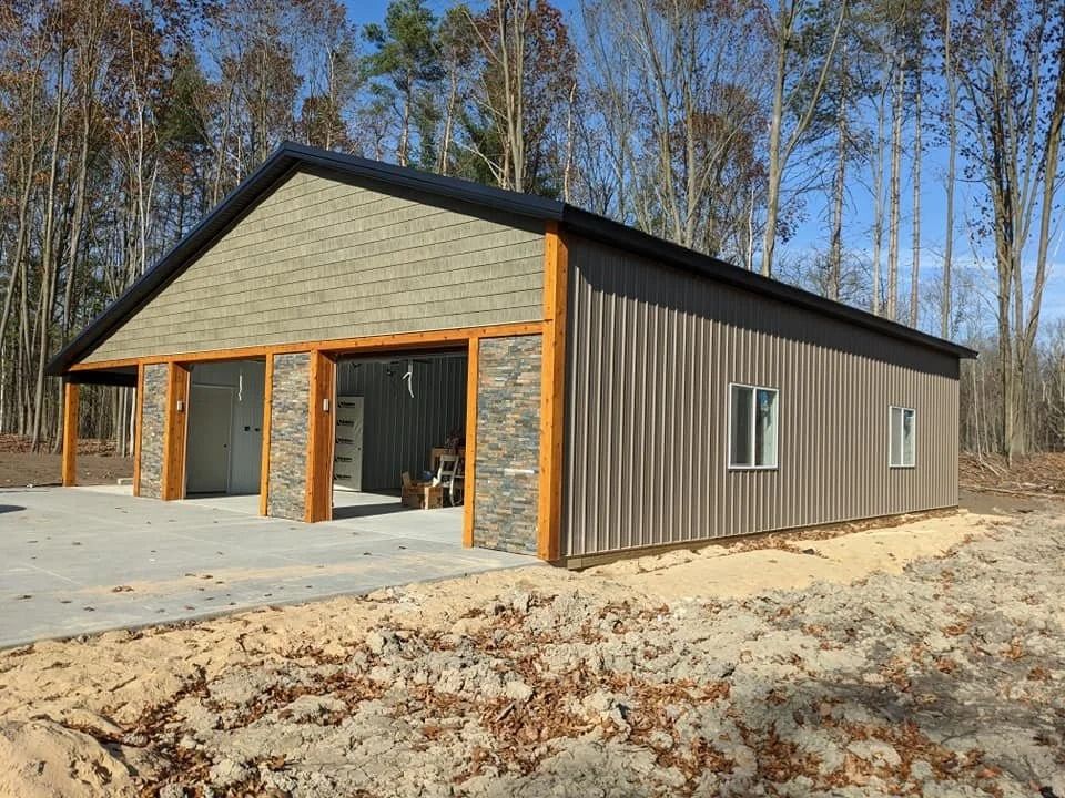 Modern barn-style building with gray siding, stone accents, and a black roof in a wooded area