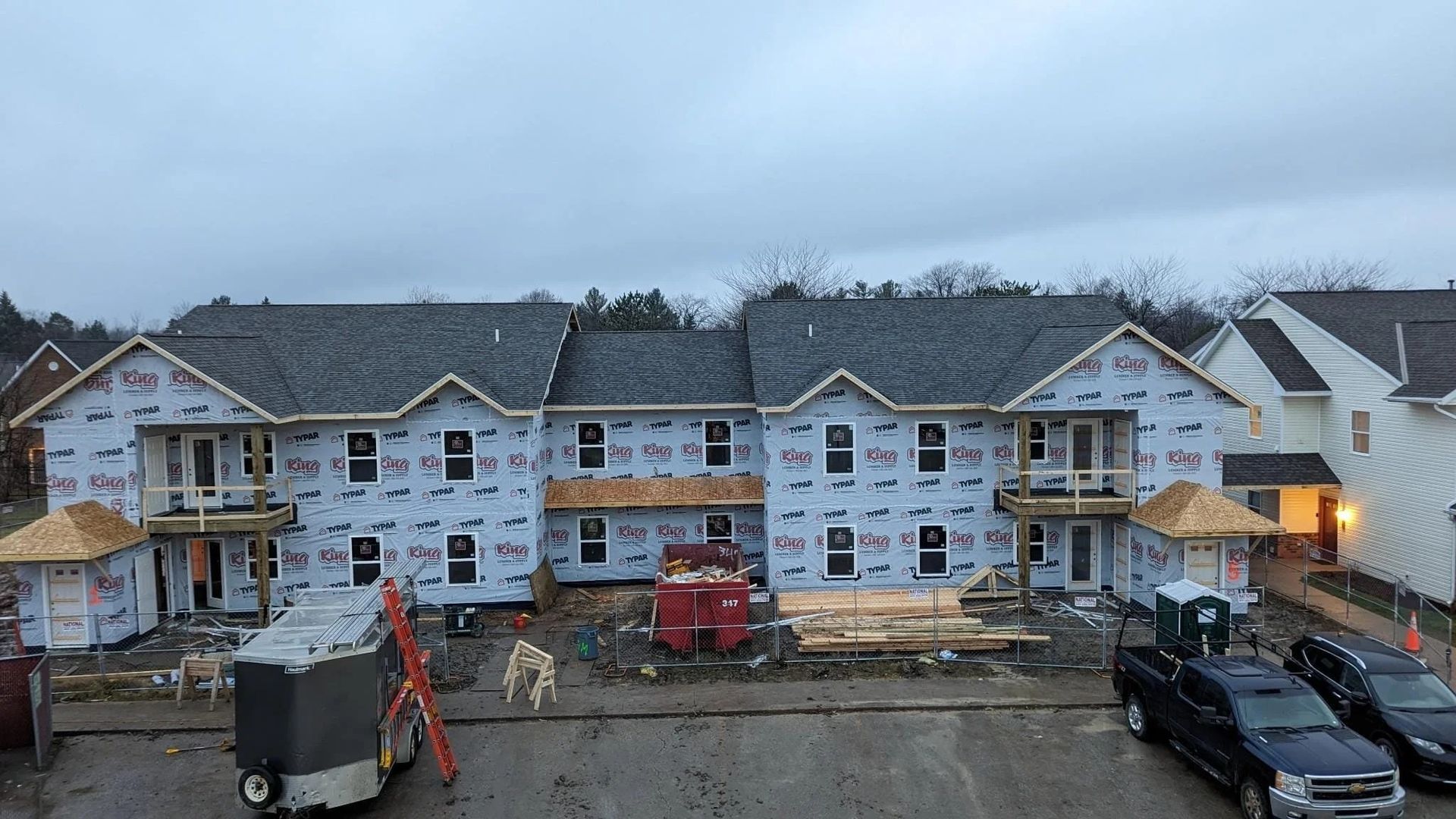 Partially built townhouse row with exposed framing, construction equipment, and parked vehicles at dusk