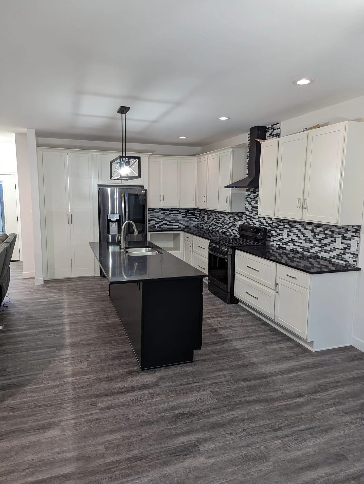 Modern kitchen with white cabinets, black island, stainless fridge, and gray wood flooring
