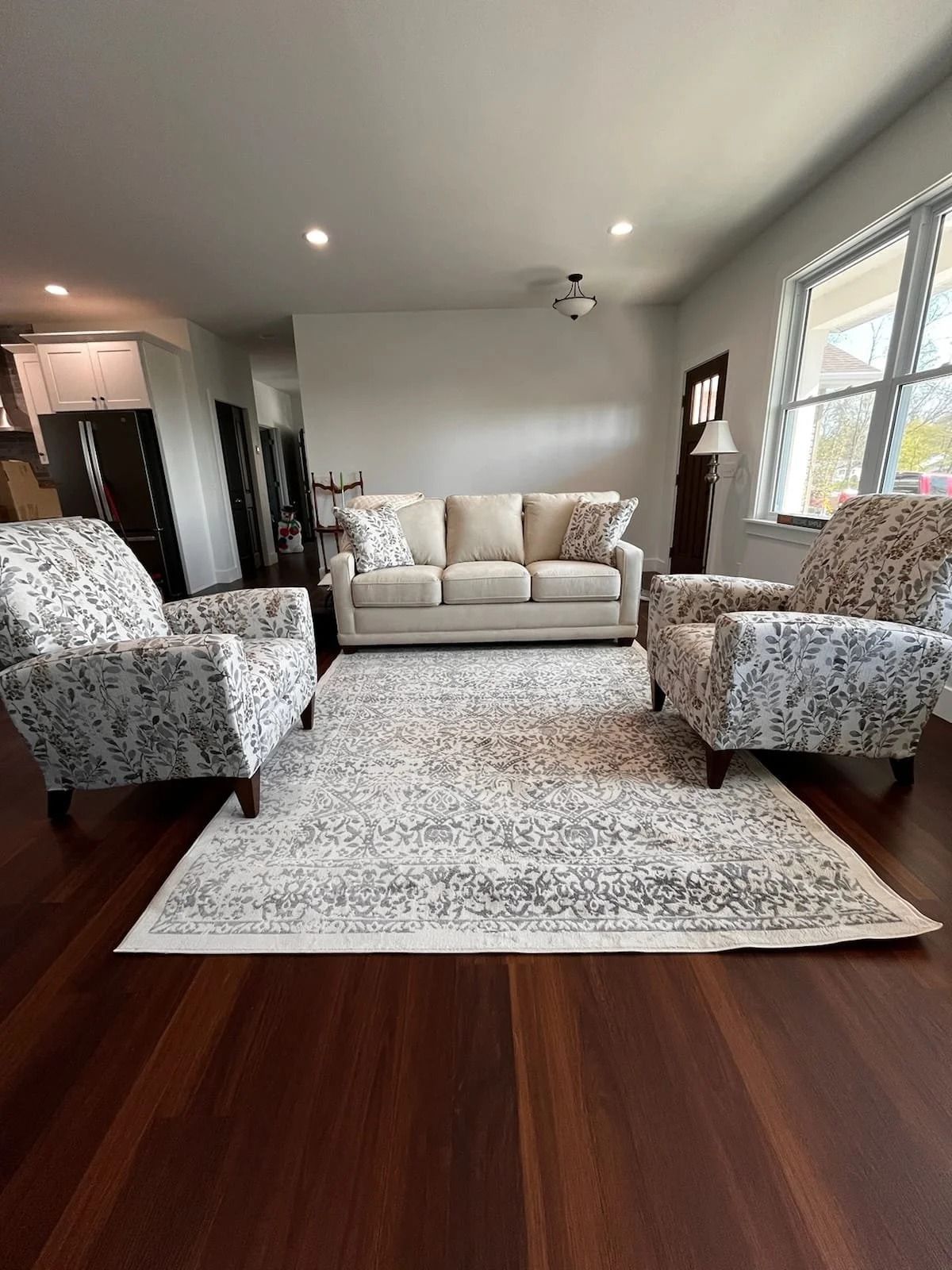Modern living room with beige sofa, patterned armchairs, and white rug on dark wood floor