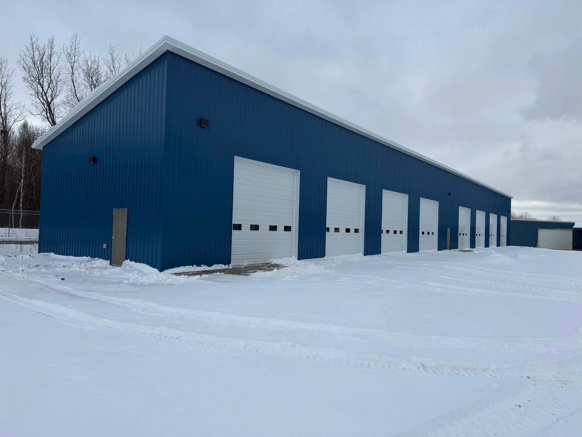 Blue metal warehouse with several white garage doors in a snowy lot