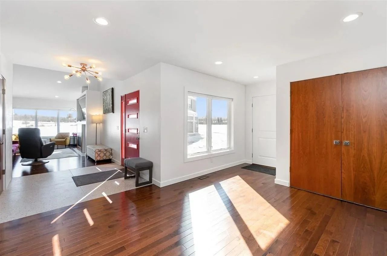 Bright empty living room with hardwood floors, large windows, and a wooden closet door.