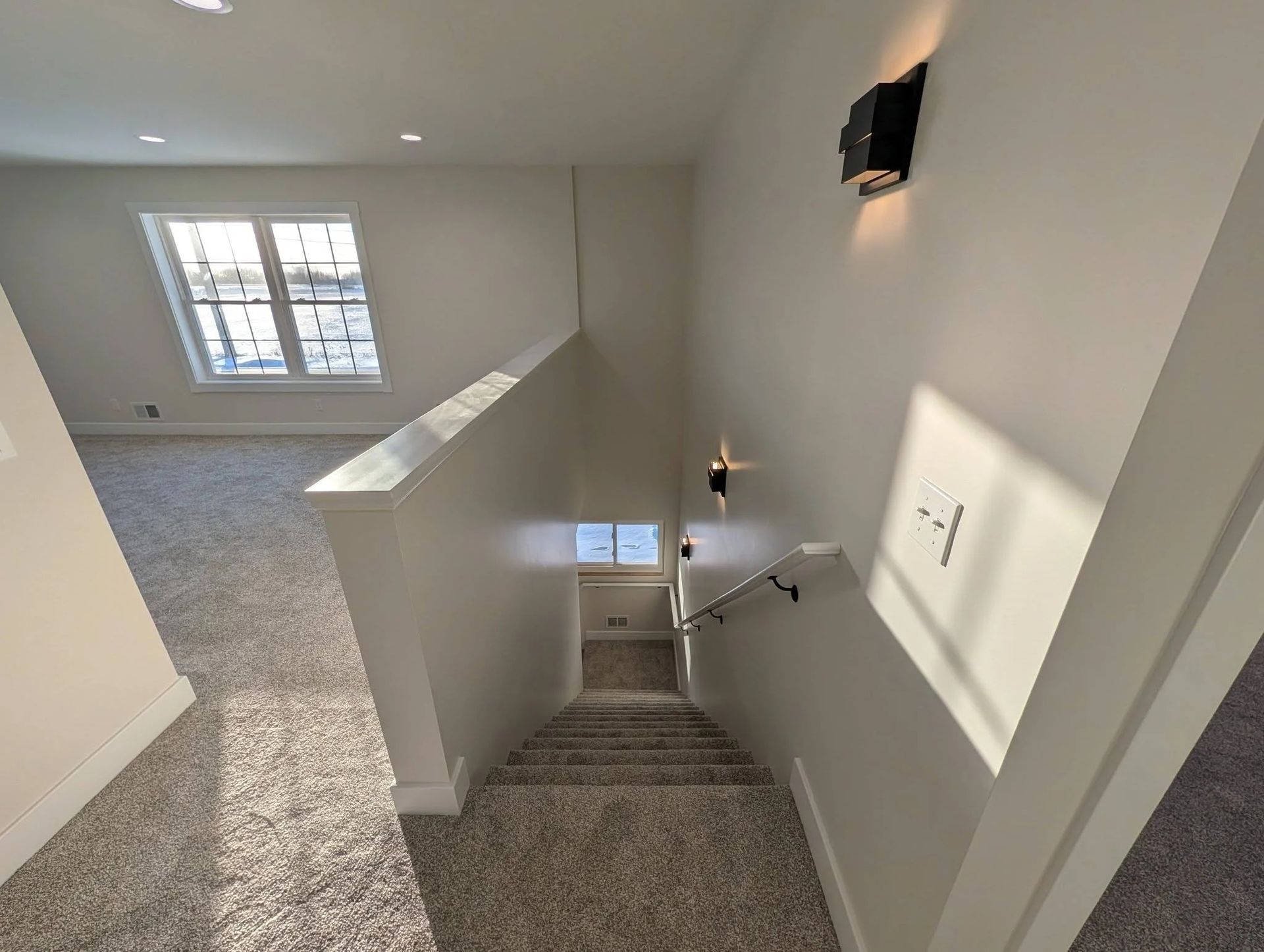 Carpeted upstairs landing and stairwell with white walls, window light, and a wall sconce.
